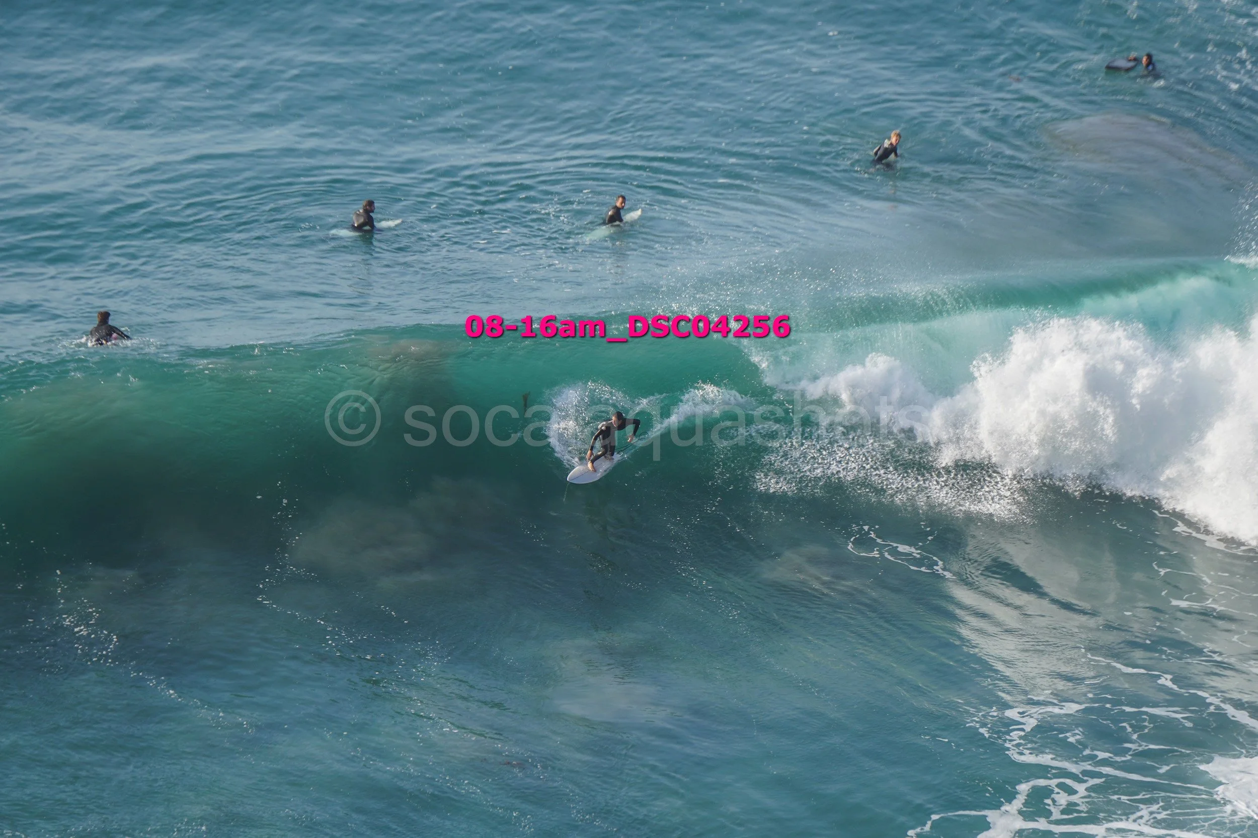 A person surfing on a wave with several other surfers in the water in the background.