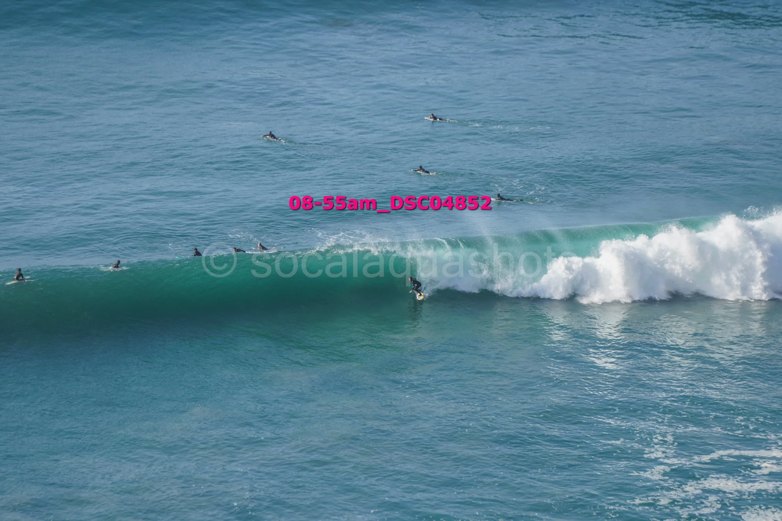A surfer riding a wave with multiple surfers in the water watching from behind.