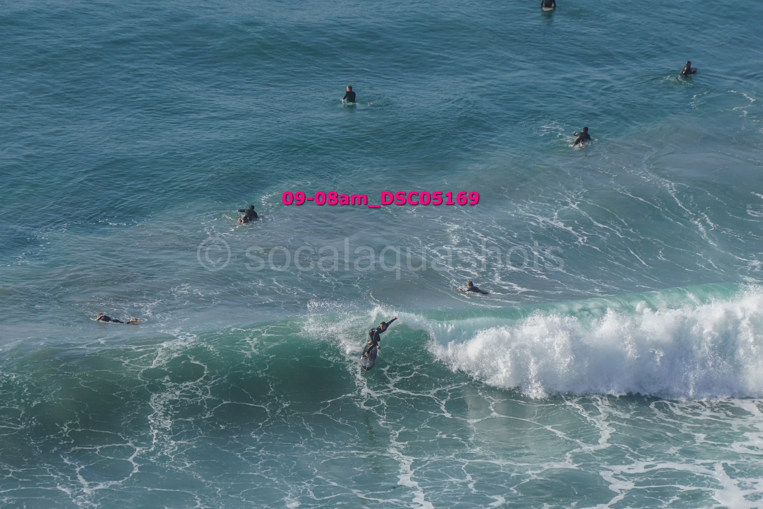 A group of surfers in the ocean, some on surfboards riding the waves and others waiting in the water.