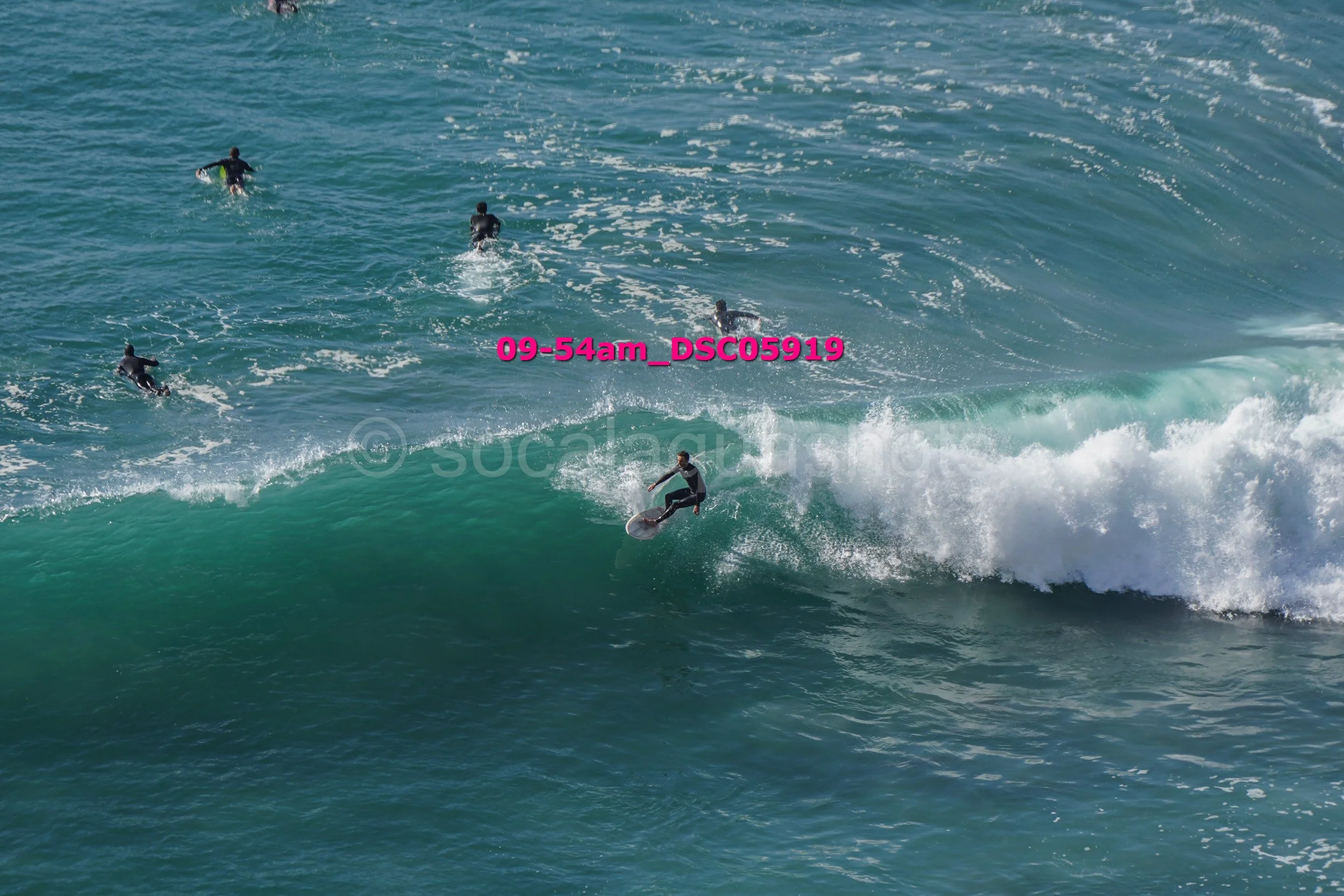 A person surfing on a wave with five other surfers in the background in the ocean.