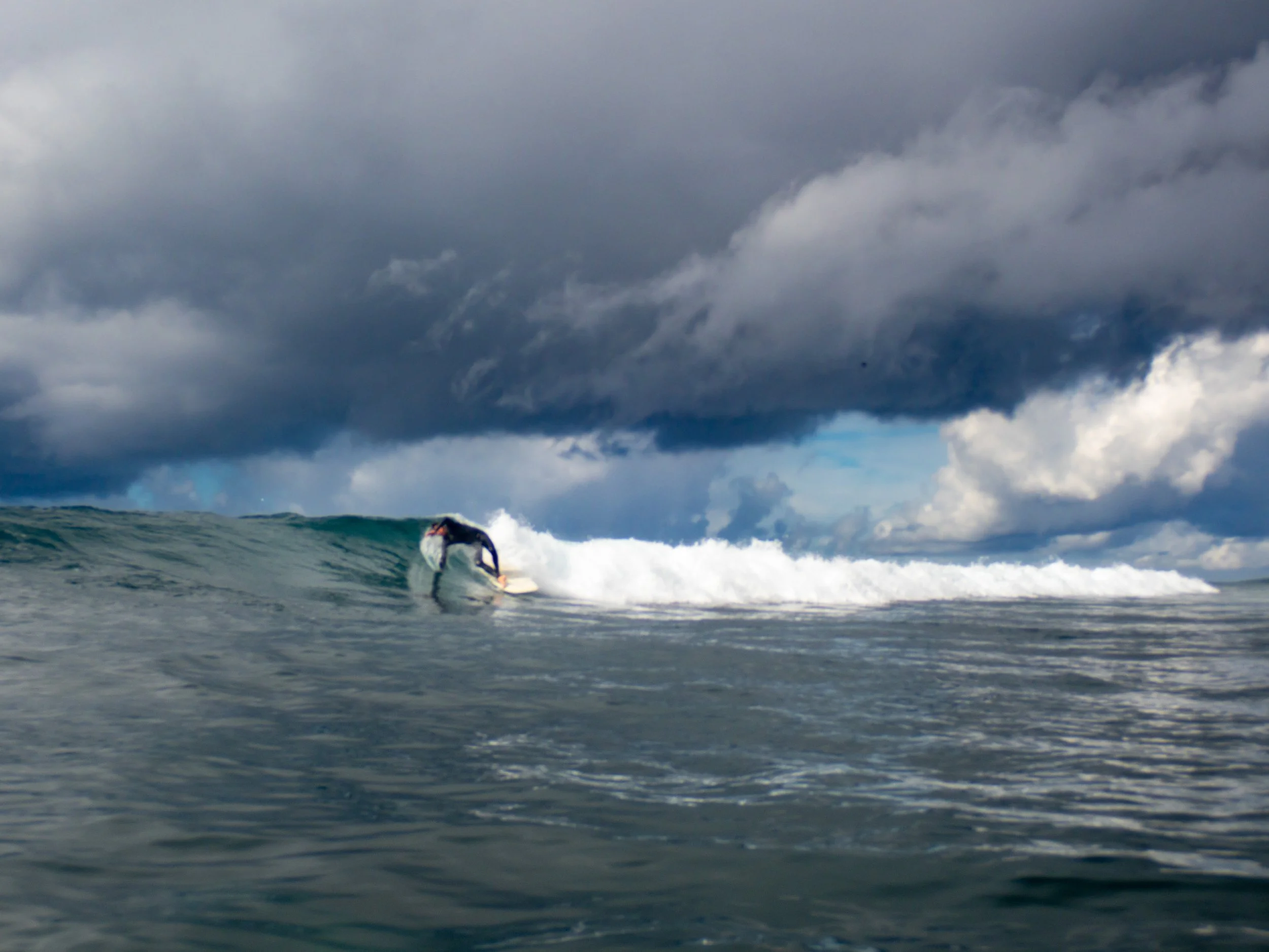 Surfer riding a wave under a cloudy sky in the ocean.