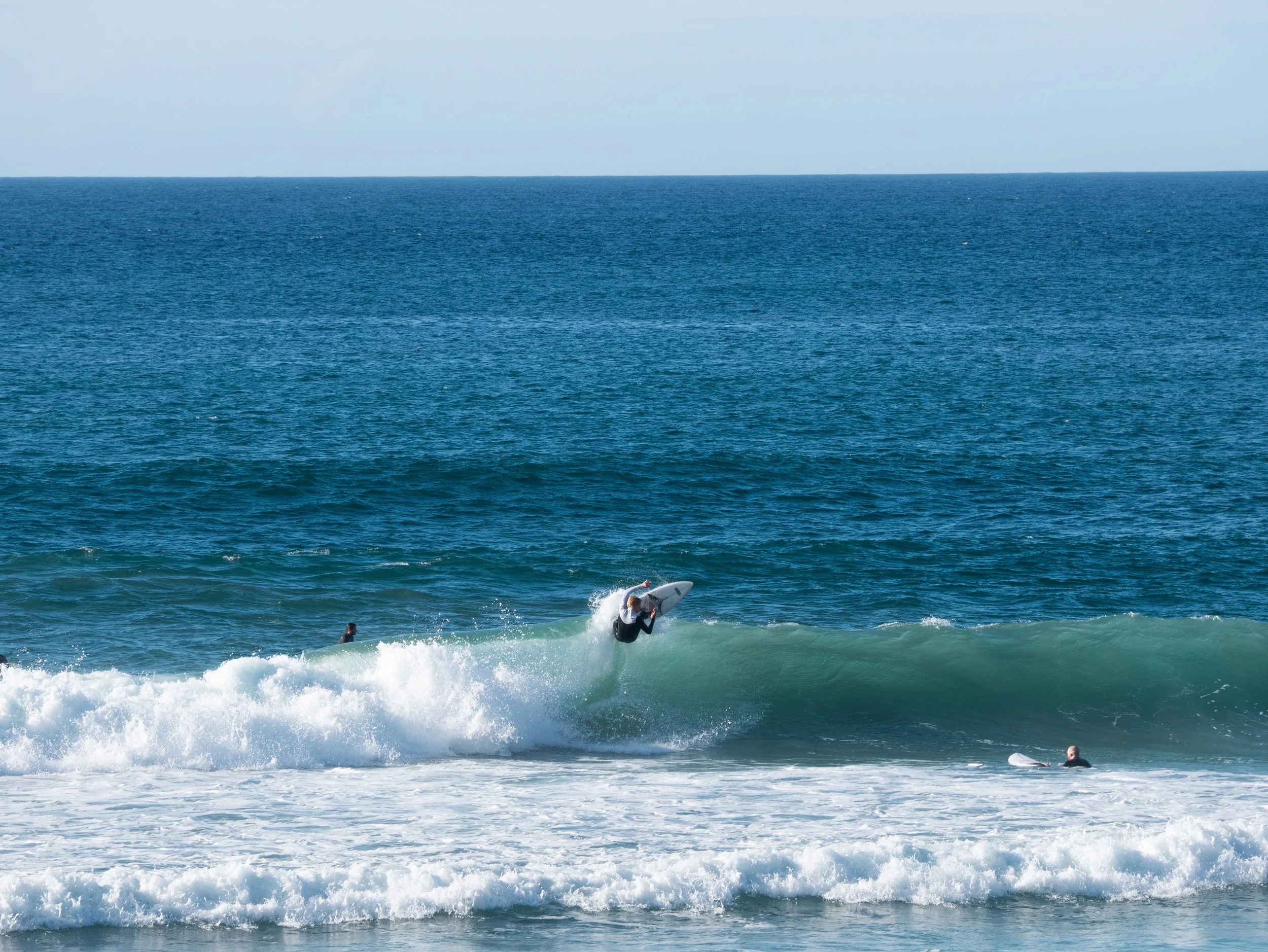 A person surfing on a wave in the ocean with other surfers nearby and the open sea in the background.