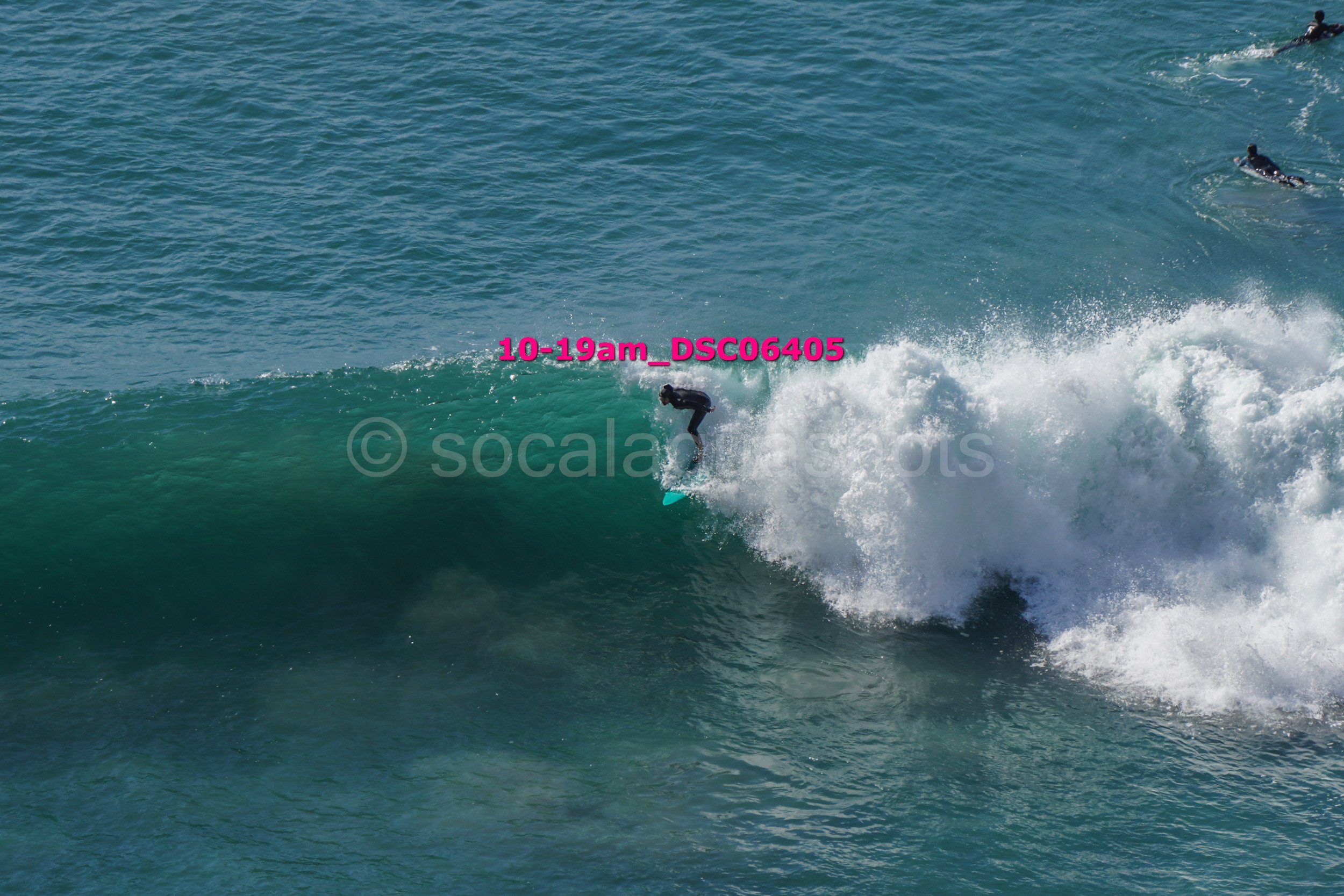 Person surfing on a wave in the ocean with two other surfers visible in the distance.