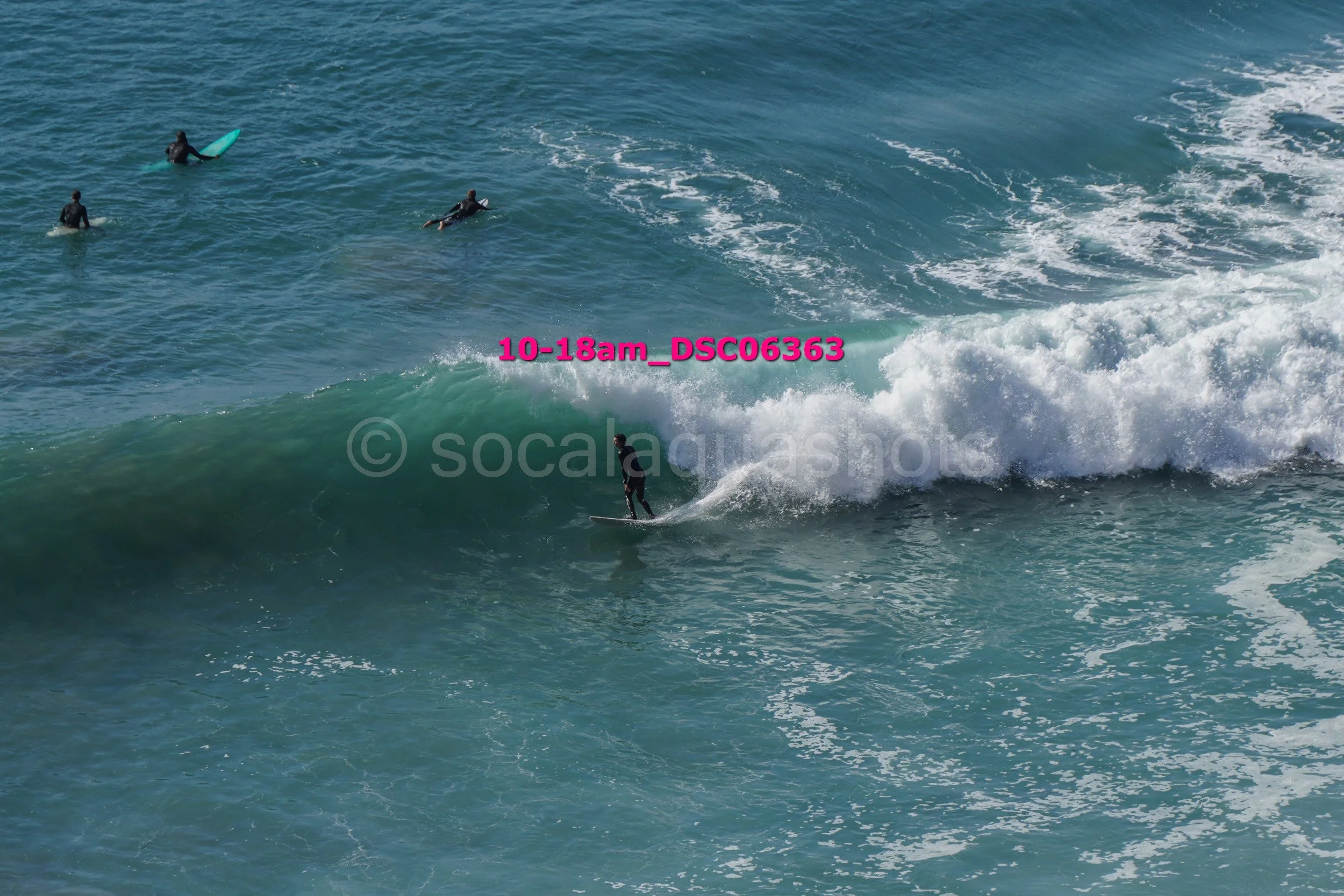 A person surfing on a wave with three others in the water nearby.