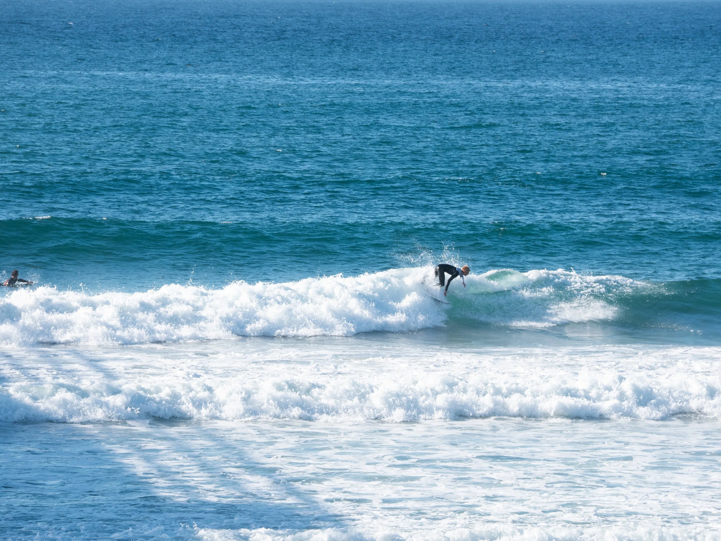 Person surfing on a wave in the ocean with another surfer in the background.