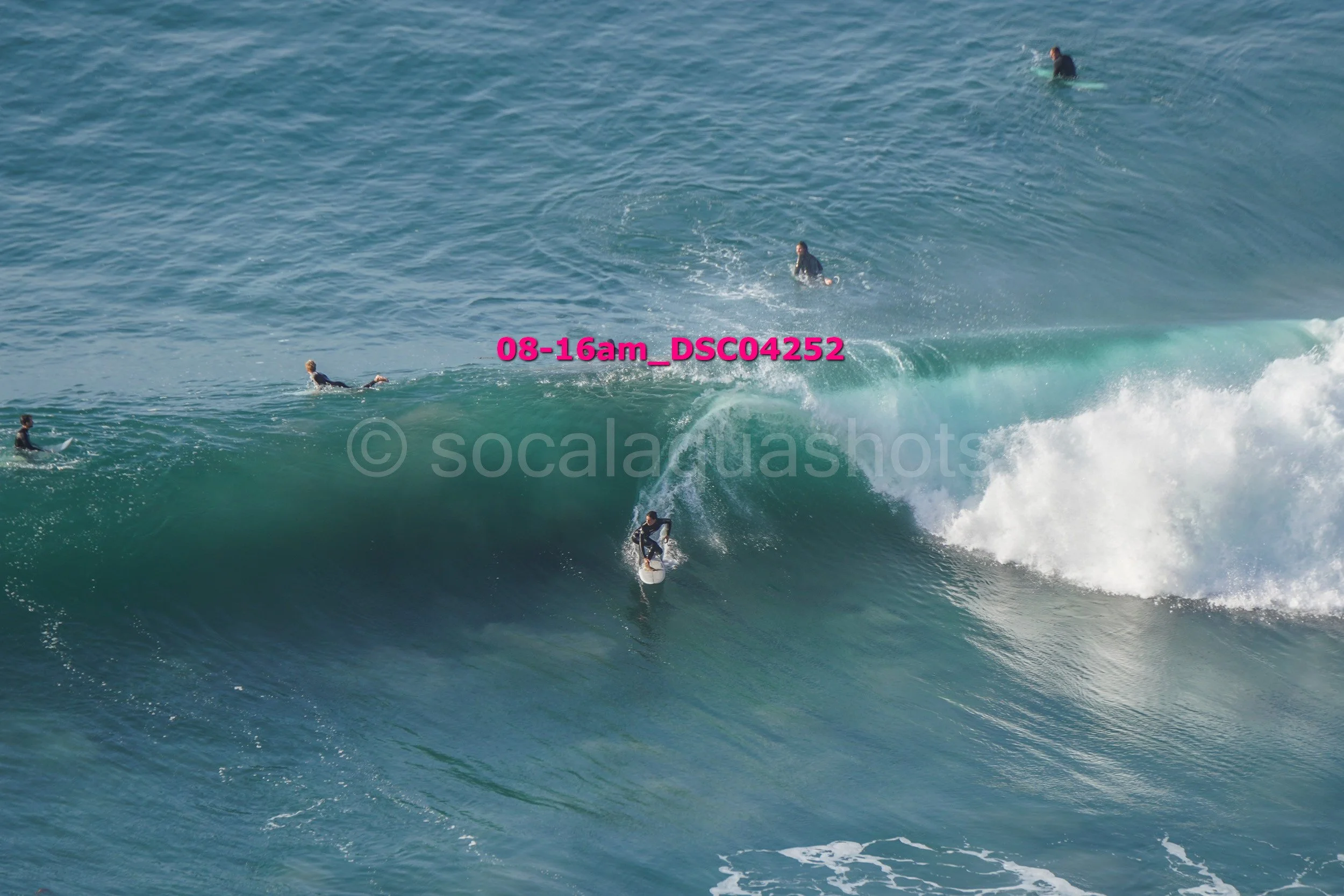 Surfer riding a large wave with several surfers in the water watching from behind.