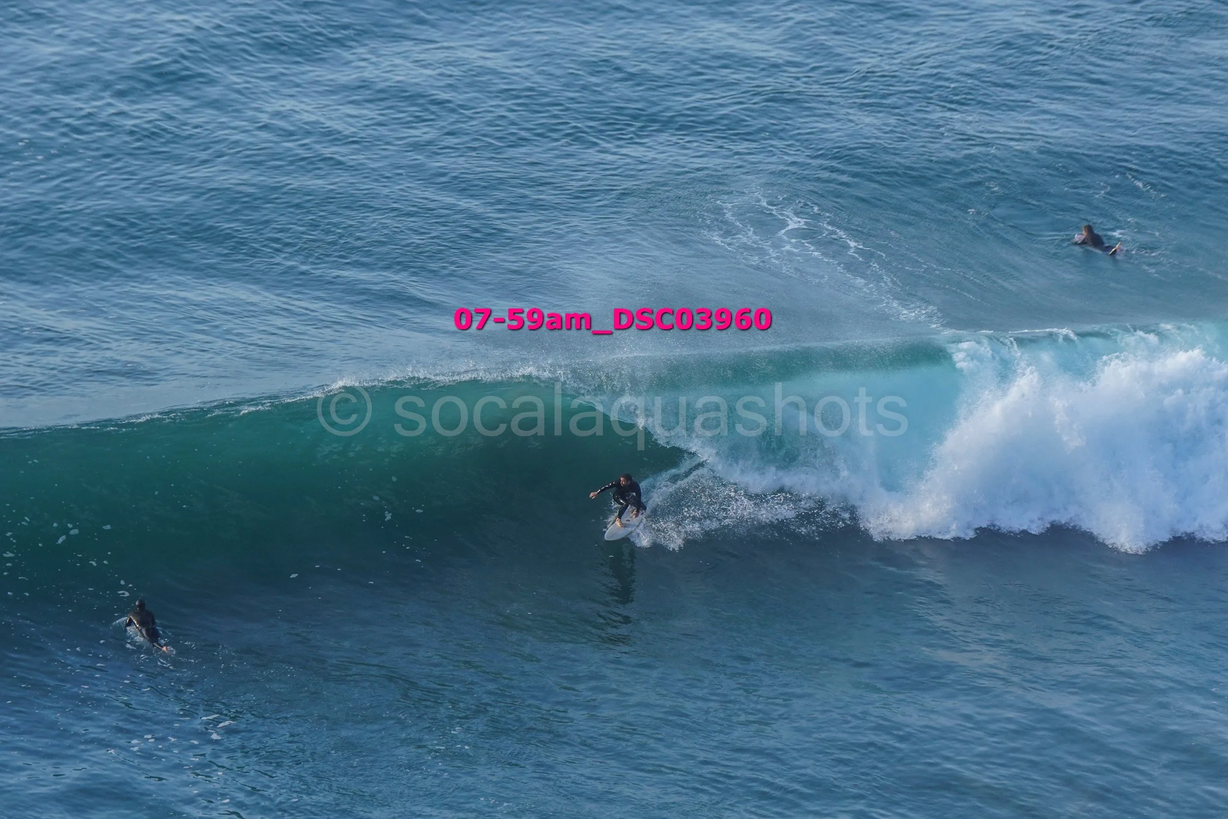 A surfer riding a large wave with two other surfers in the water nearby.
