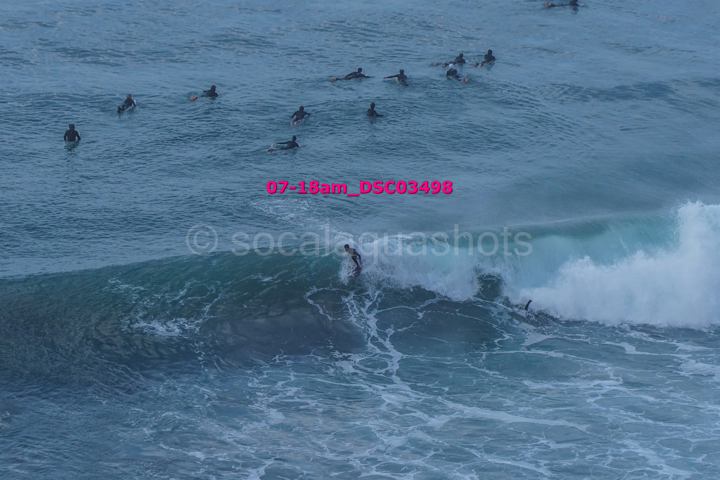 A surfer riding a wave with multiple people swimming and surfing in the background on the ocean.