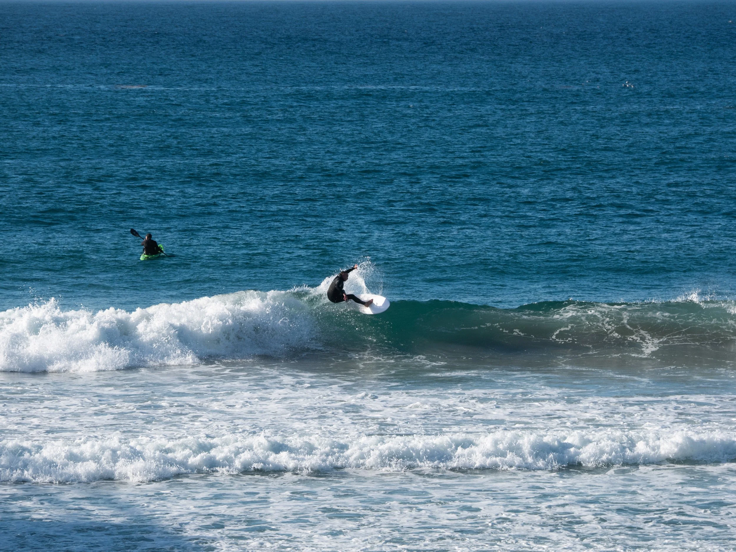 Two surfers in wetsuits riding waves in the ocean, with the water extending to the horizon.