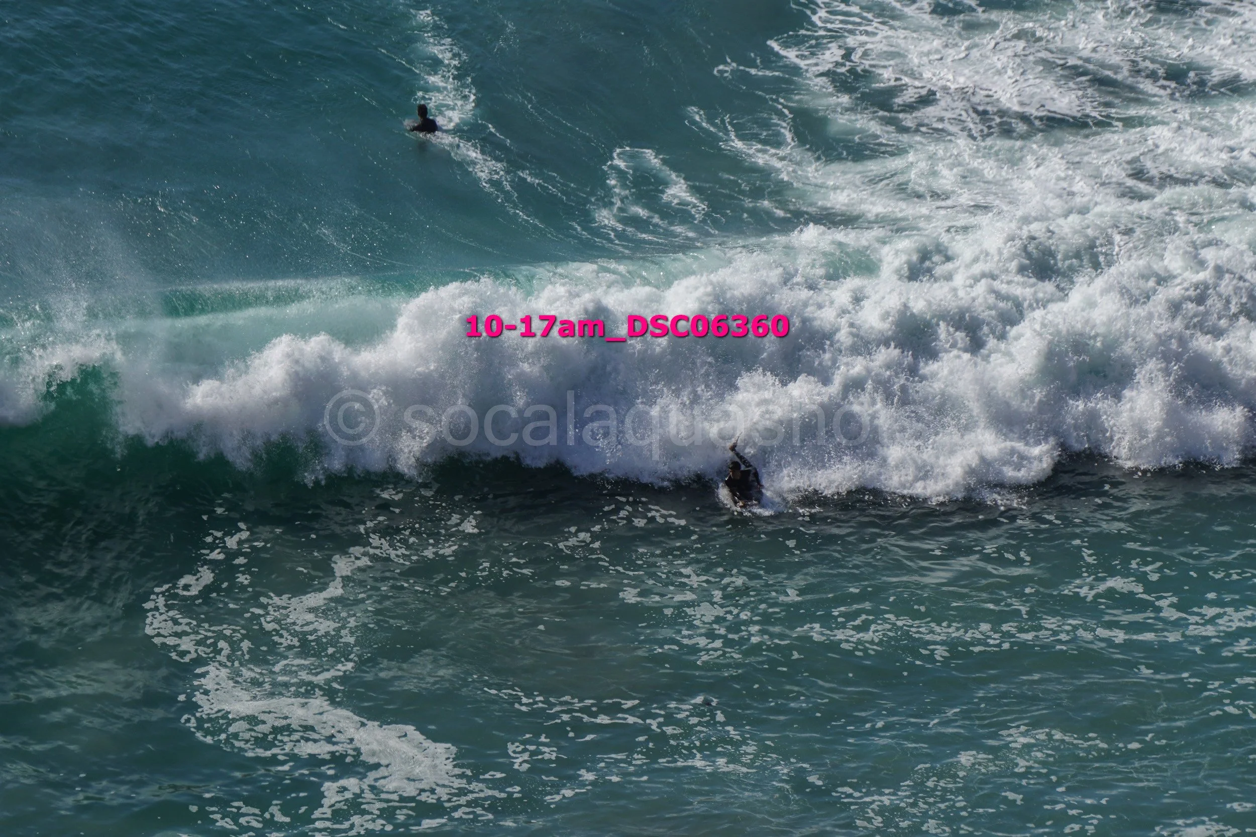 A person surfing on a wave in the ocean with another surfer visible in the distance.