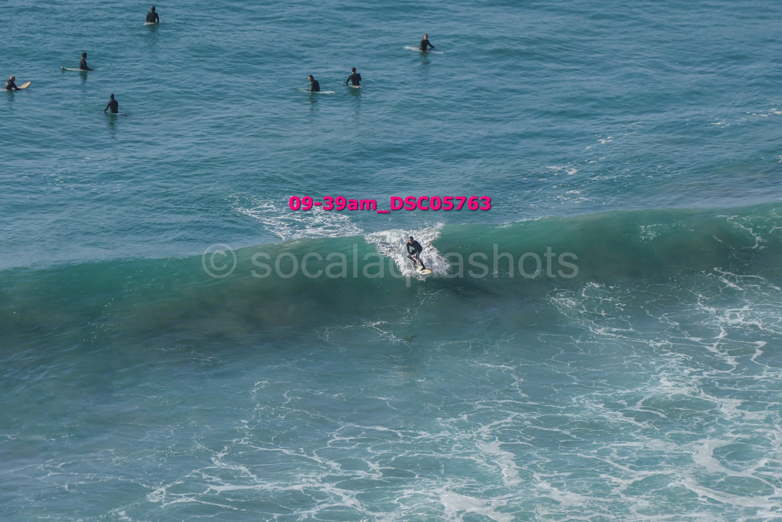 A person surfing on a wave in the ocean with multiple surfers in the background.