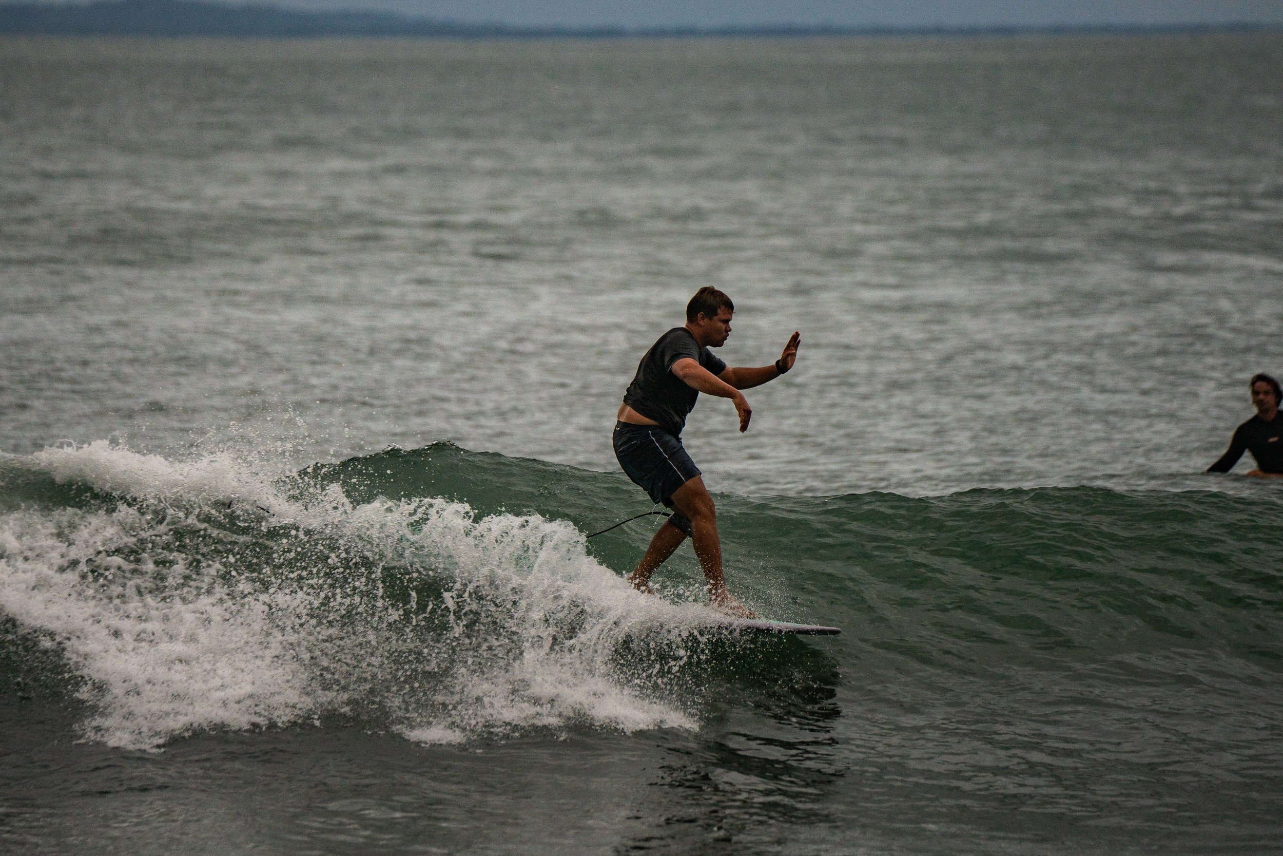 A person surfing on a wave in the ocean, with another person visible in the background.