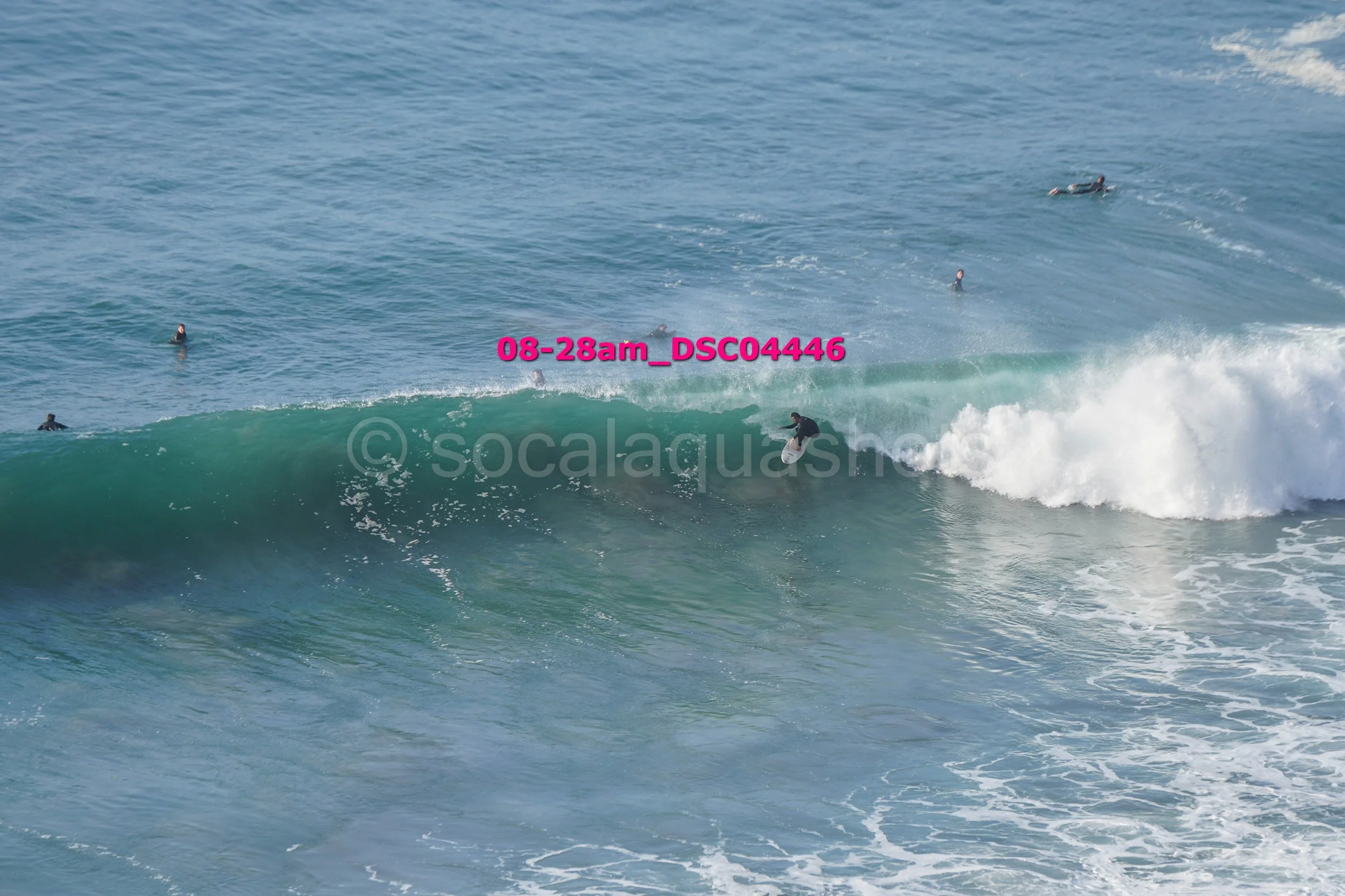 A person surfing a wave in the ocean on a clear day with several other surfers in the water