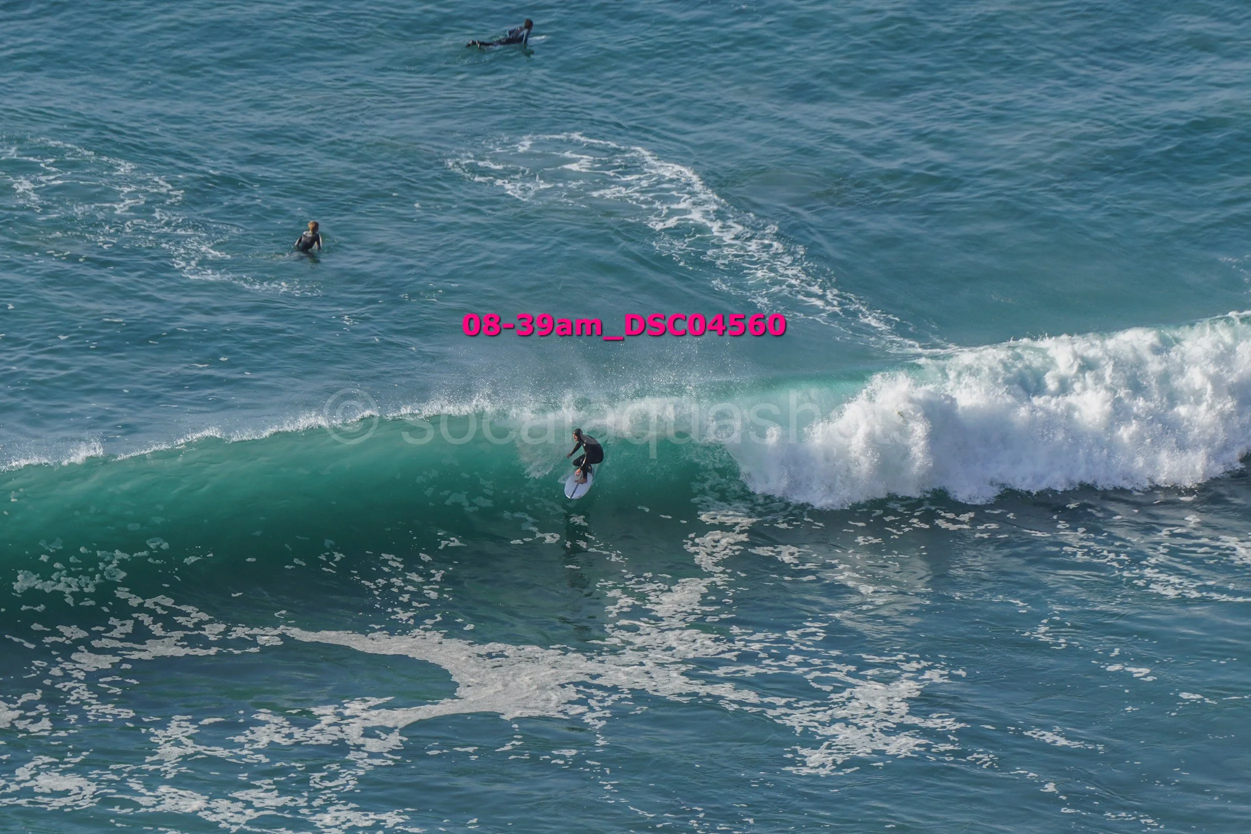 Surfer riding a wave in the ocean with three other surfers in the water nearby