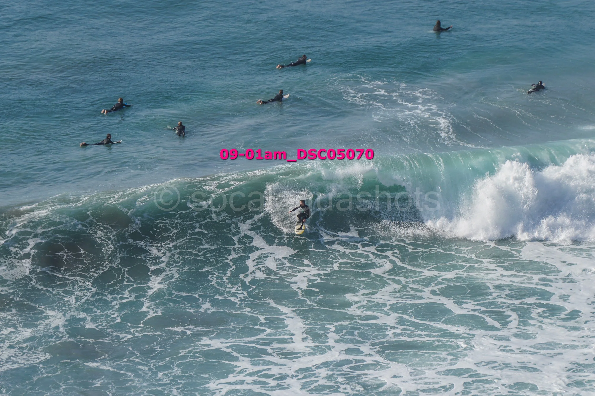 A person surfing on a wave with several other surfers in the background in the ocean.