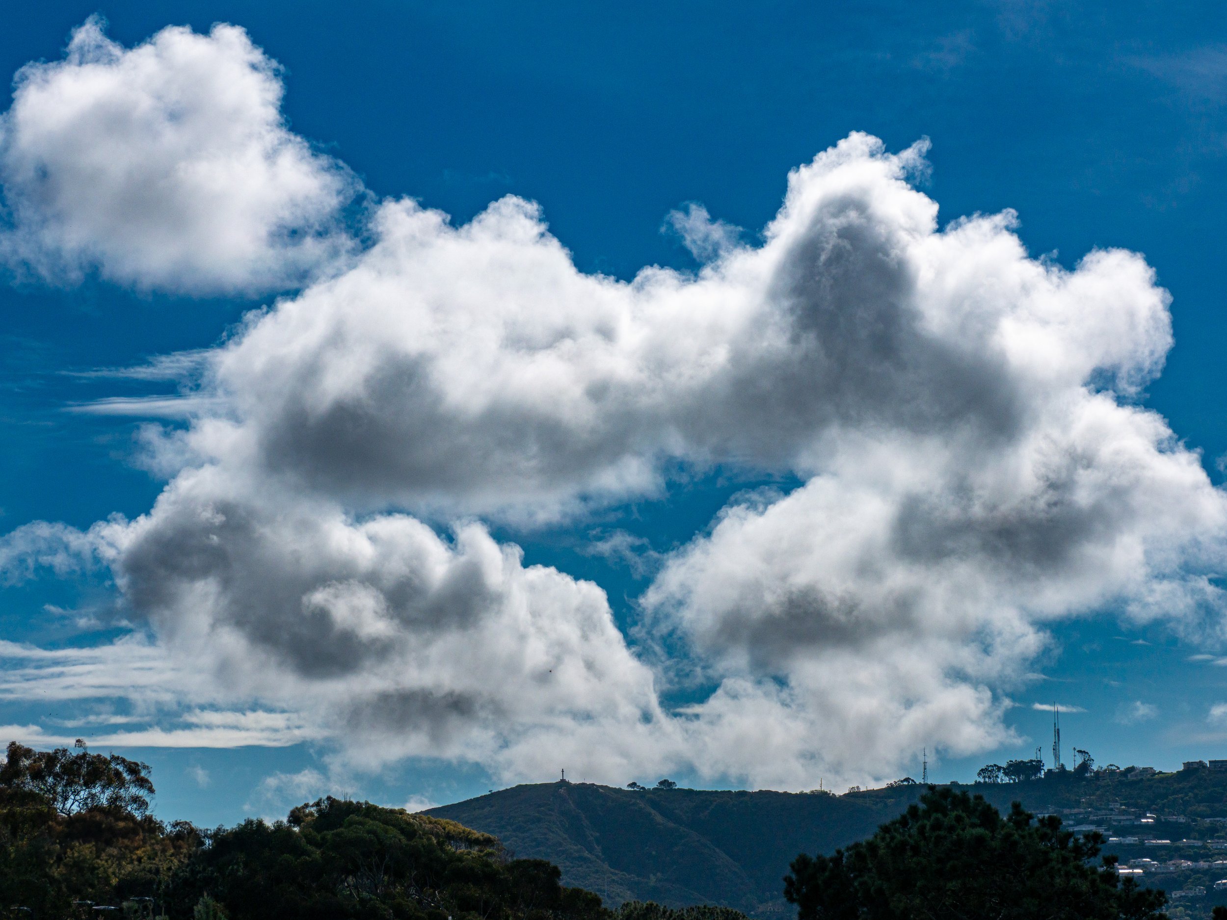 Cloudy sky over a hilly landscape with trees and communication towers.
