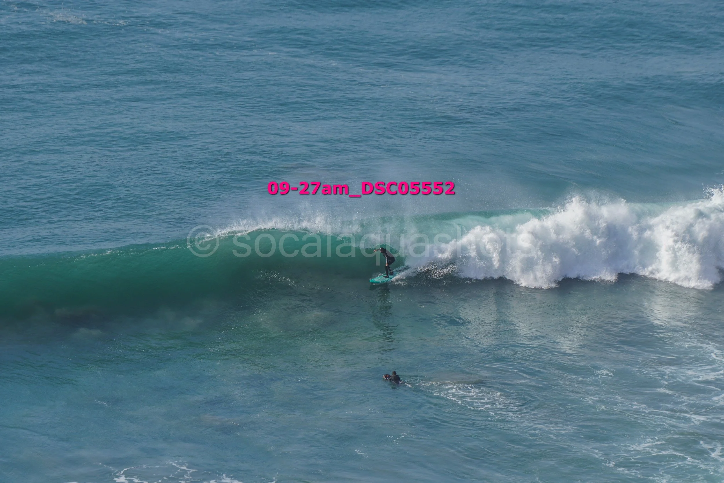 A person surfing on a wave in the ocean with a drone capturing the scene.