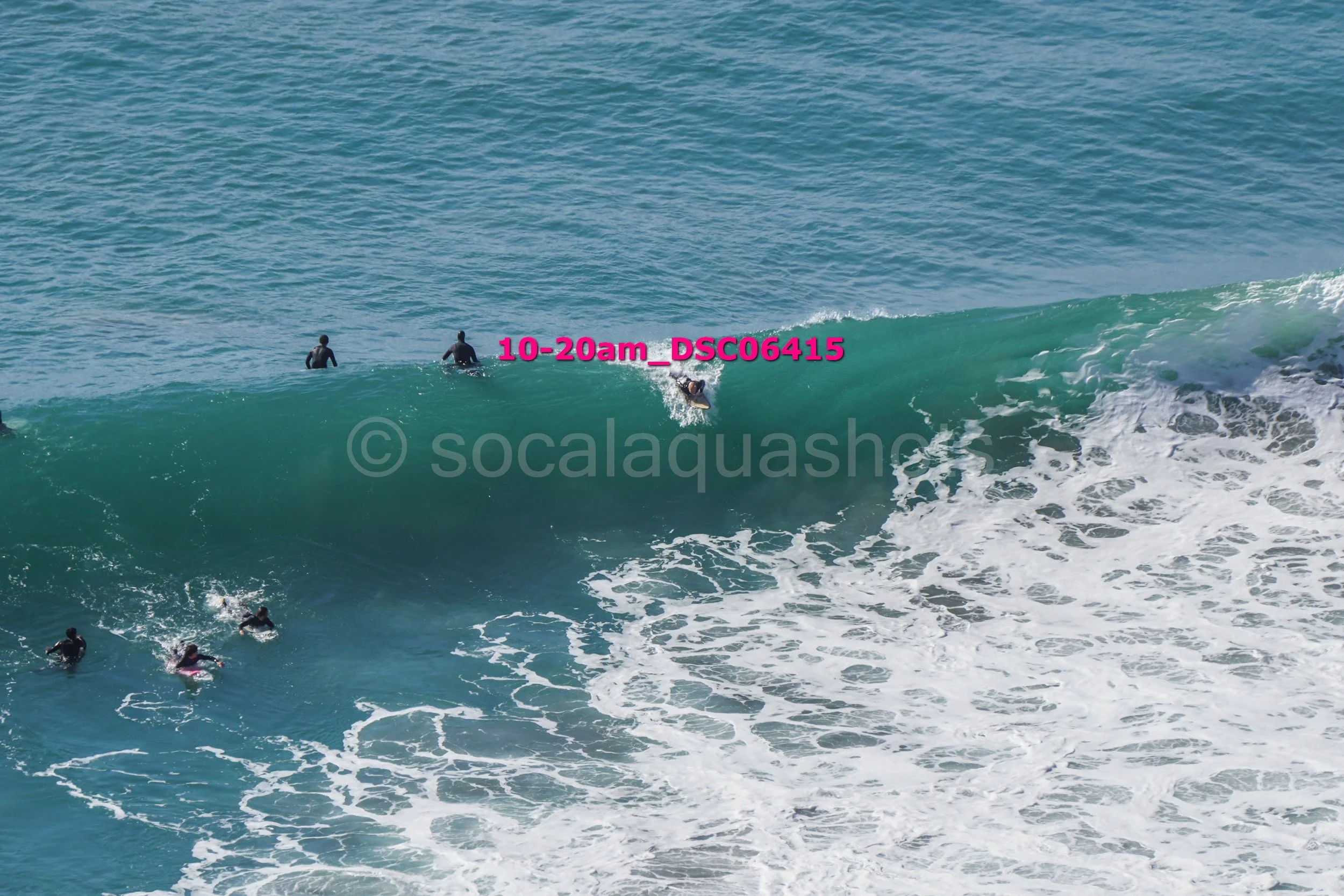 A group of people in wetsuits surfing on large ocean waves with a few people in the water watching or waiting.