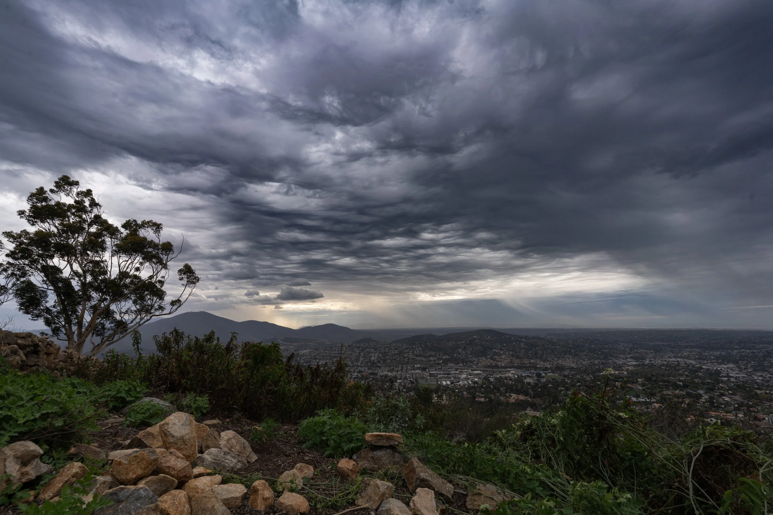 A landscape view of a city with mountains in the distance under a cloudy, stormy sky.