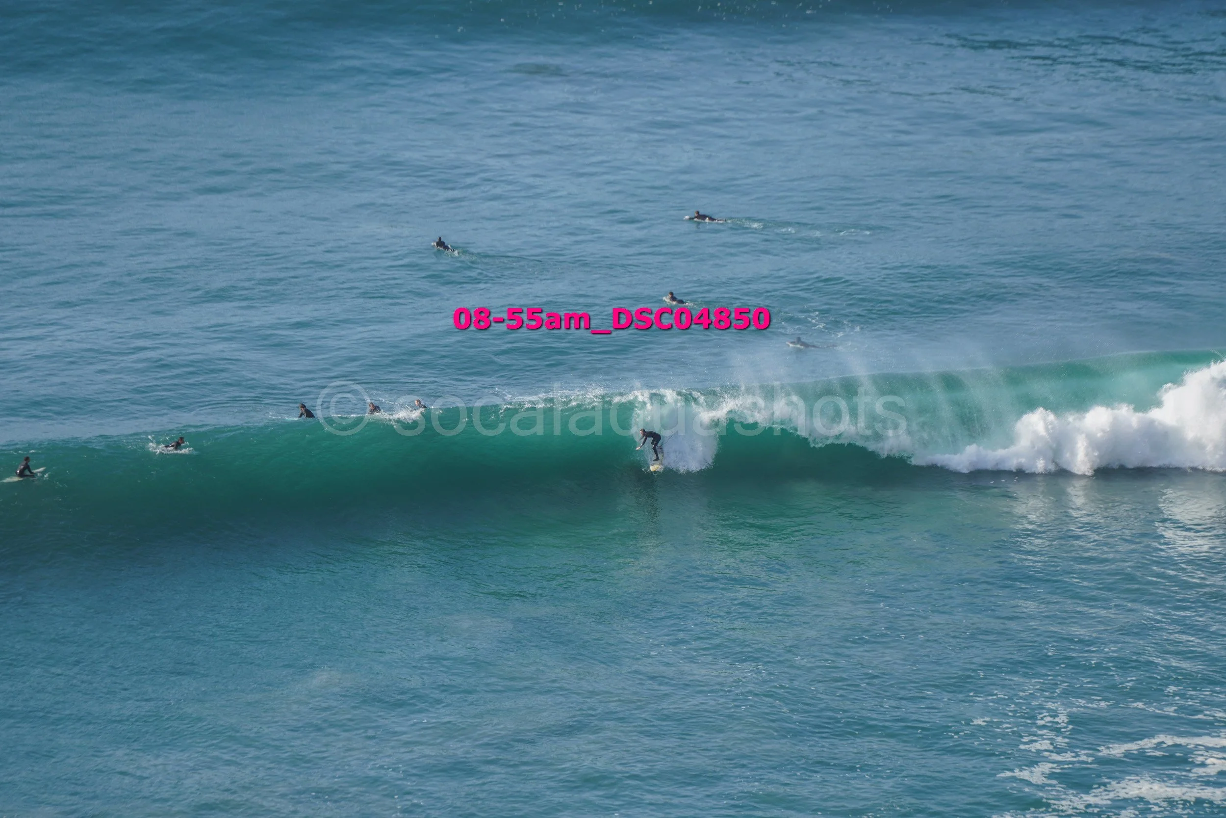 A person surfing a large wave with multiple surfers in the water around.