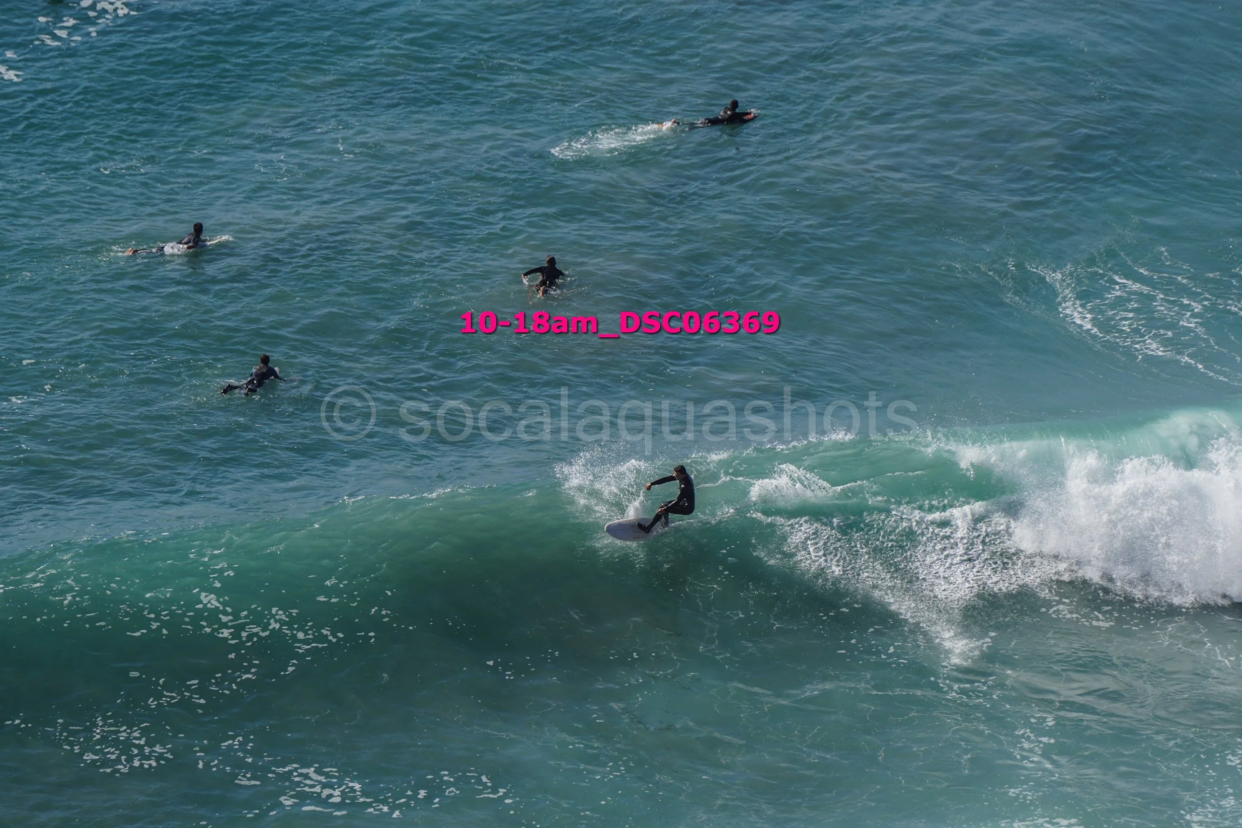A person surfing on a wave with several others swimming or surfing in the water nearby.