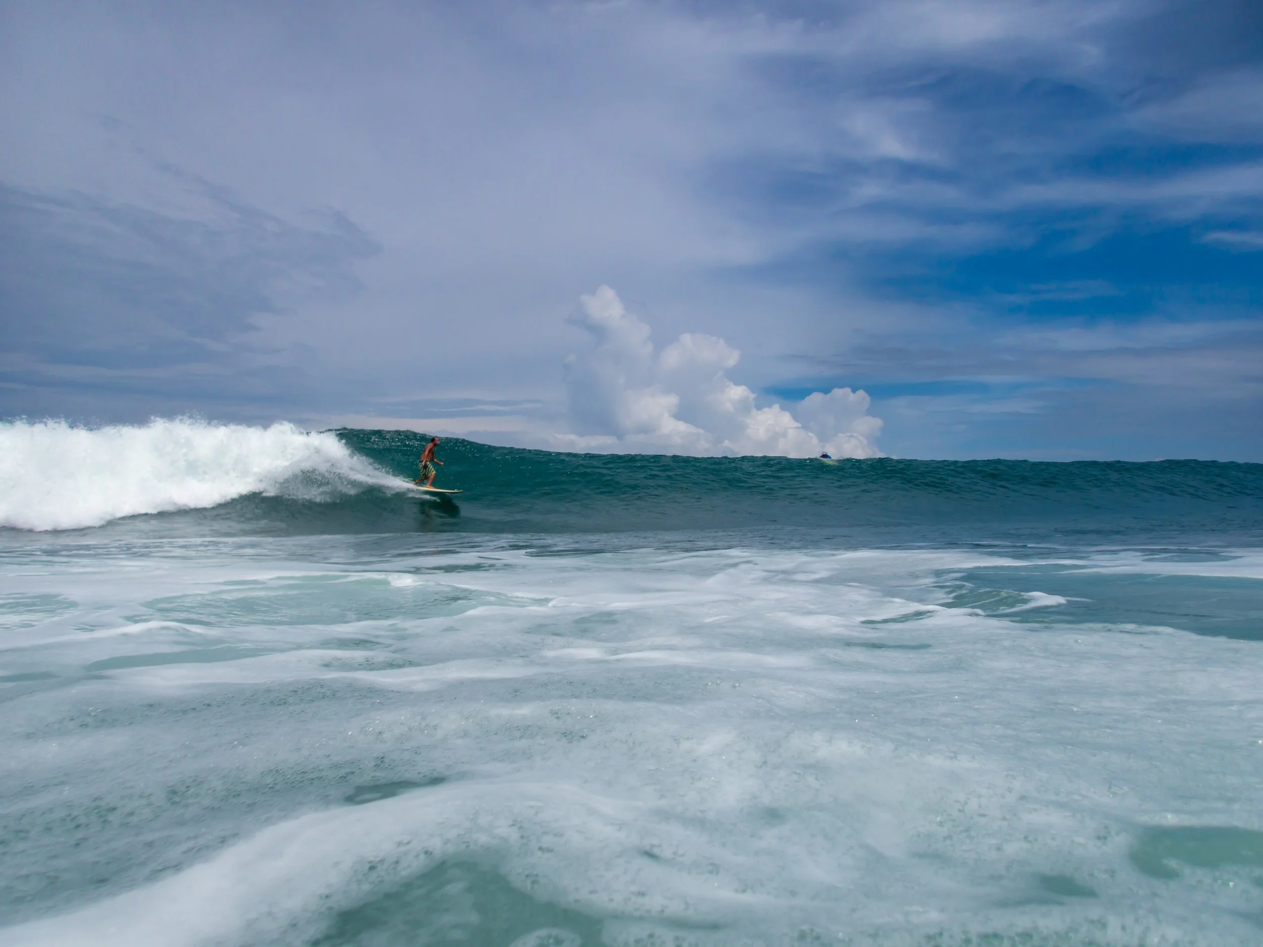 Surfer riding a wave in the ocean with cloudy sky