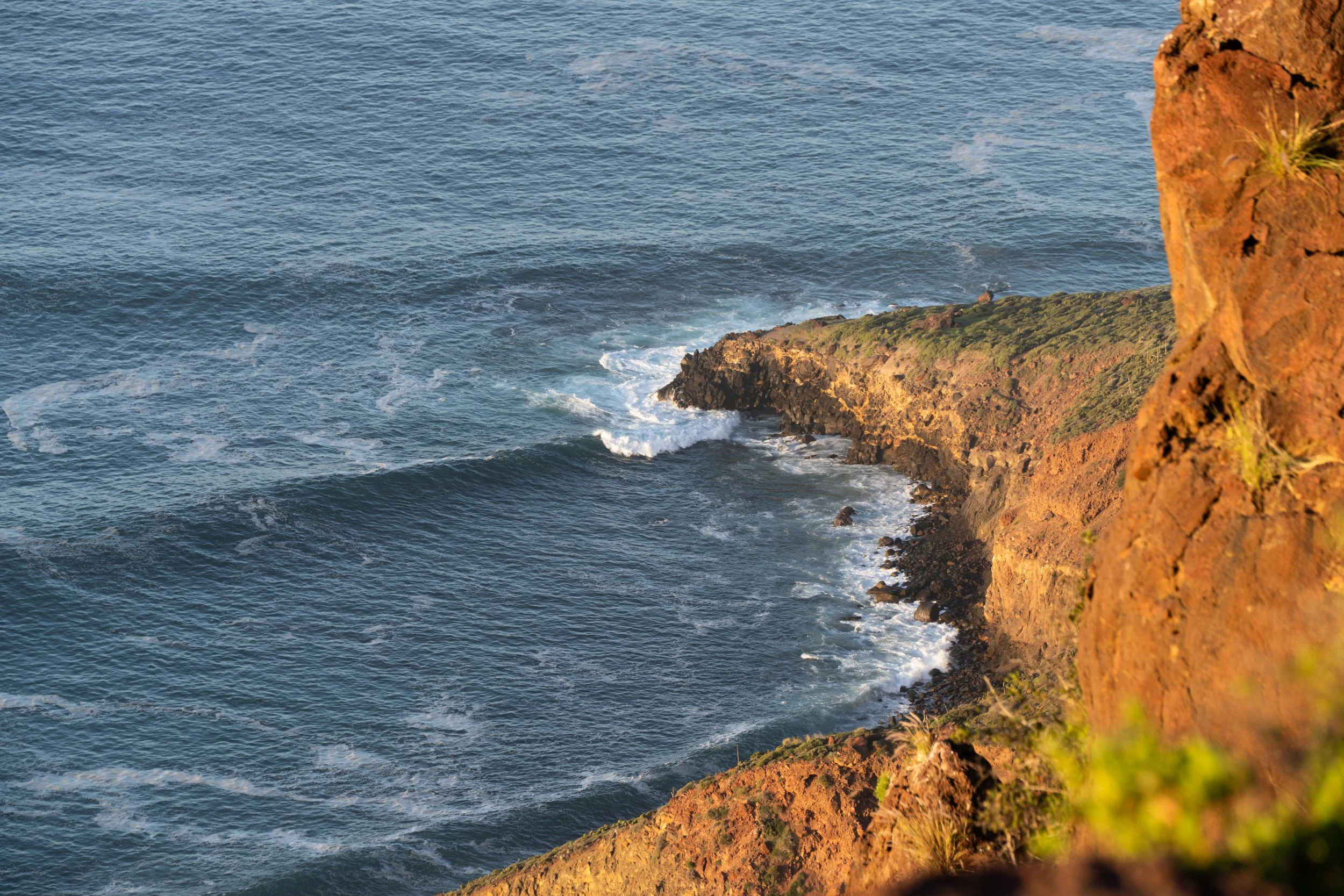 Ocean waves crashing against a rocky cliff side during sunset.