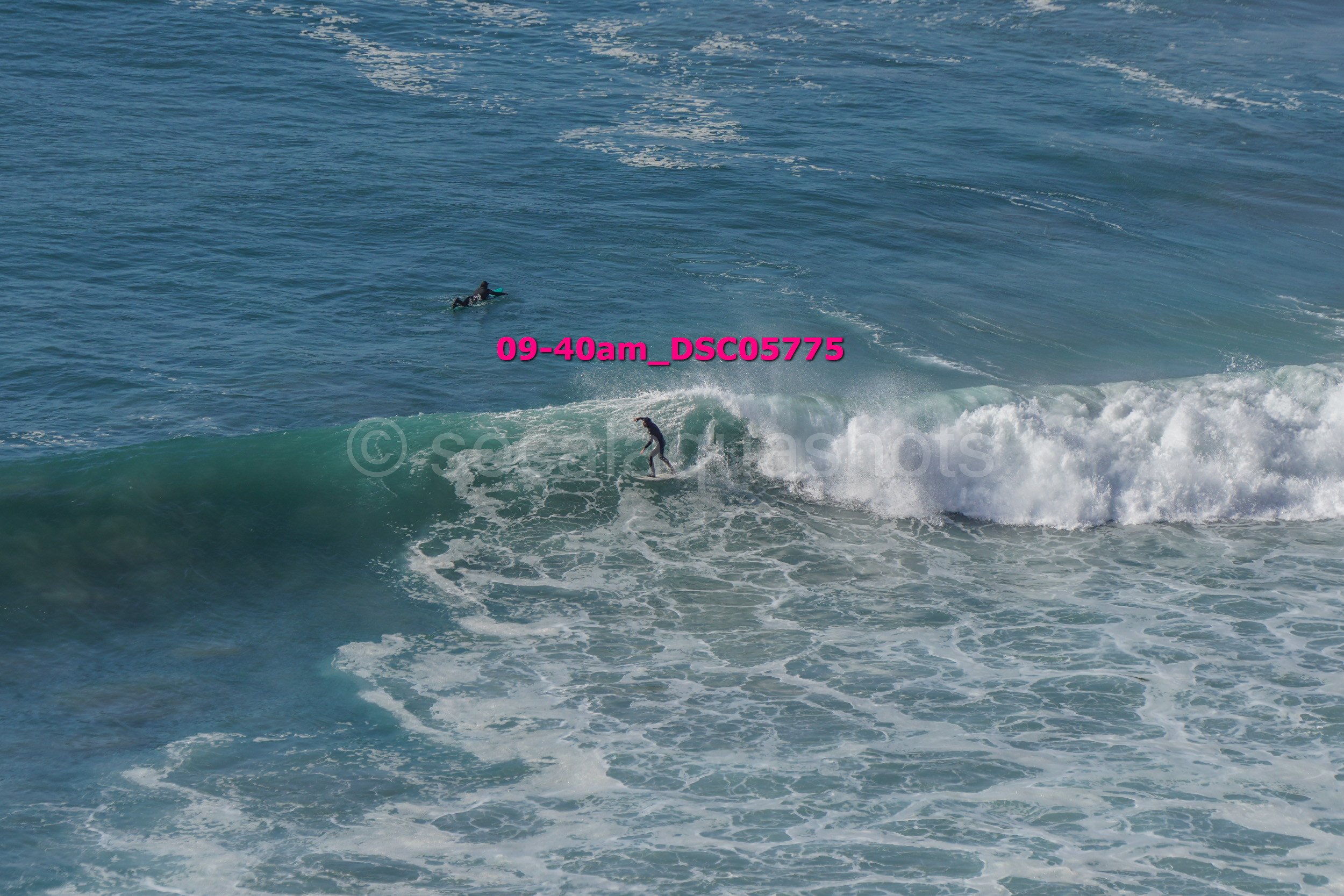 A person surfing on a wave in the ocean with another person swimming in the background.