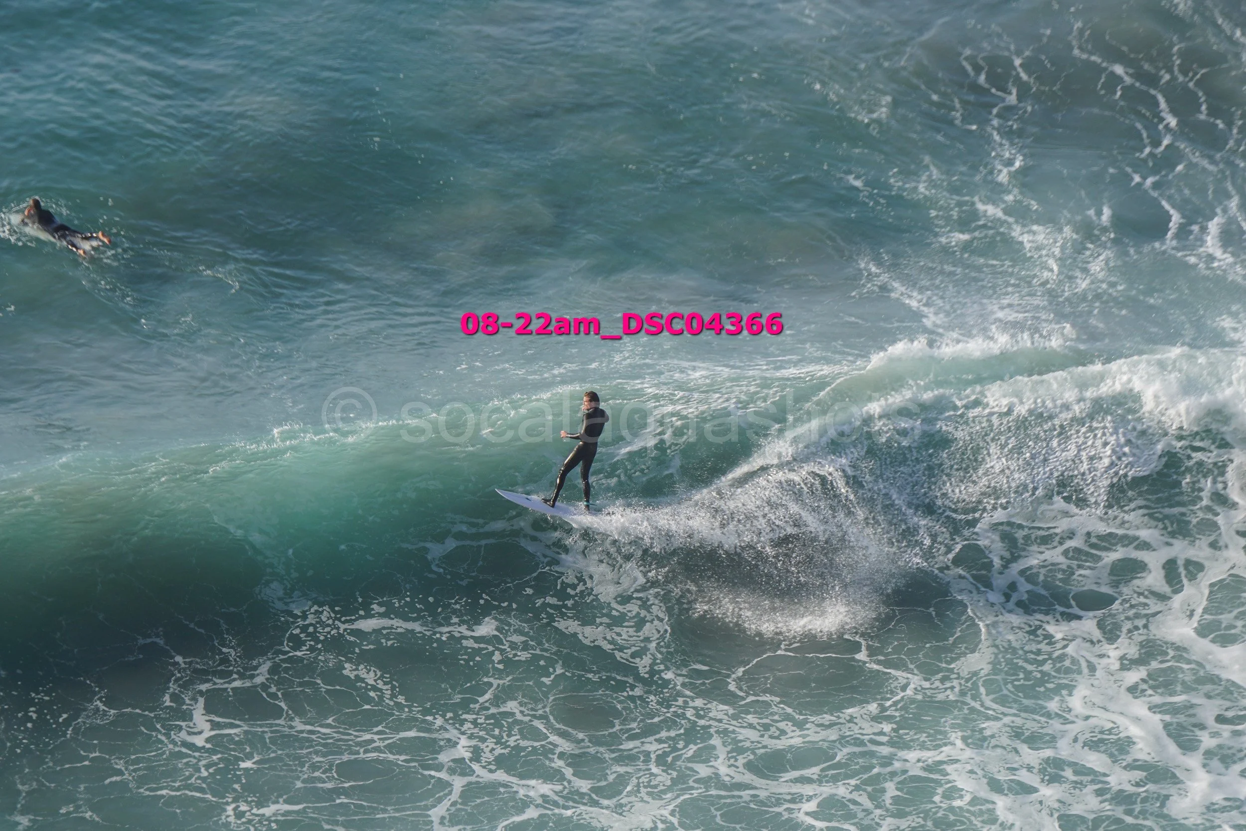 A person surfing on a wave in the ocean with another swimmer swimming nearby.