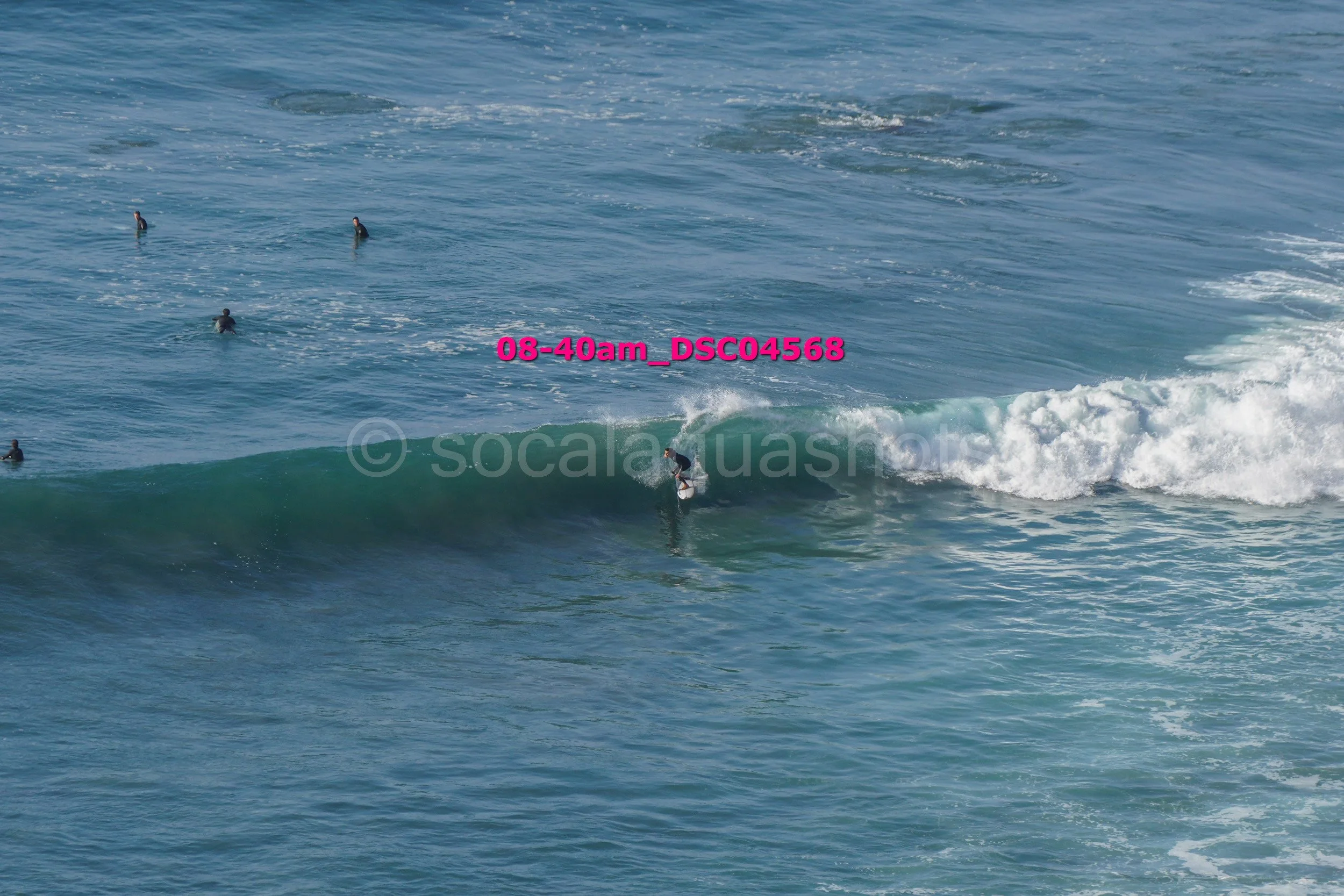 A person surfing on a wave in the ocean with several other surfers in the water nearby.