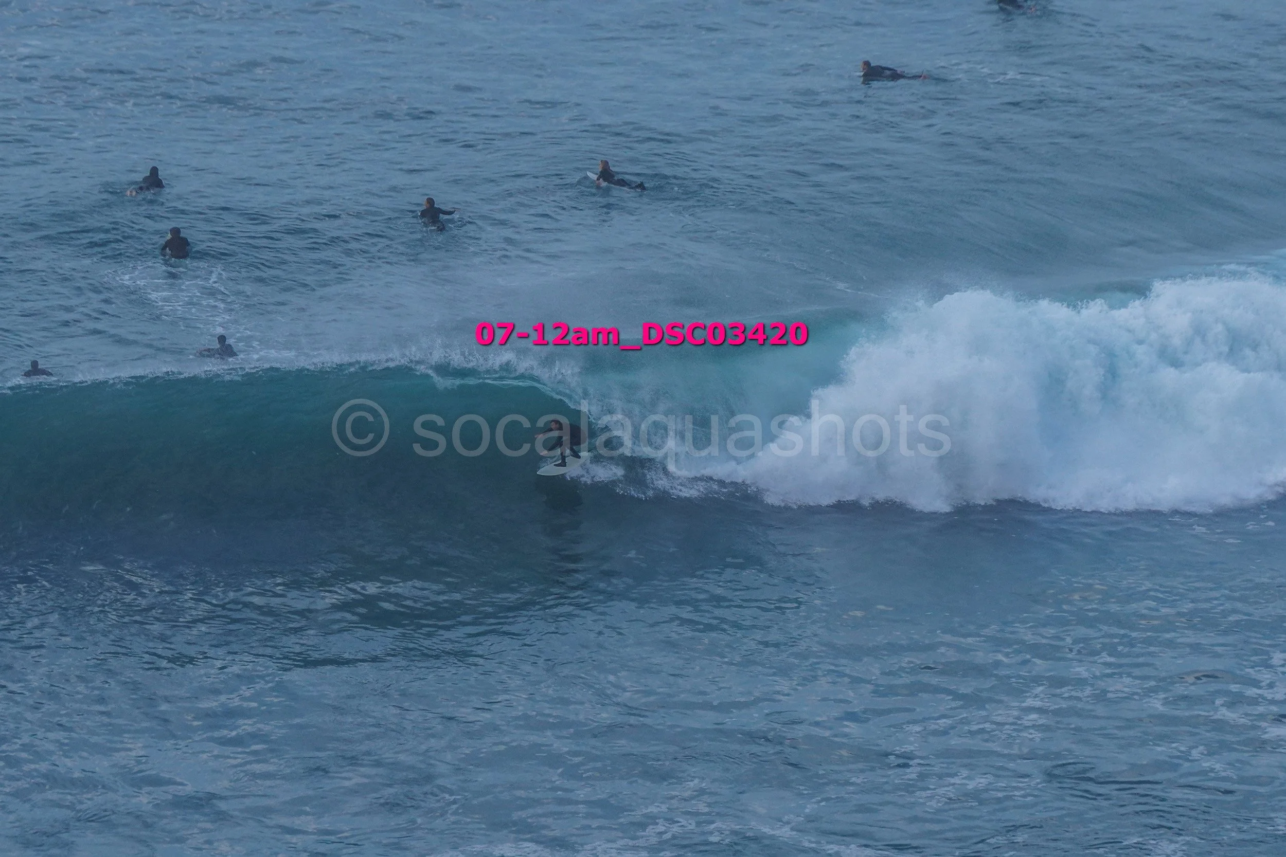 Surfer riding a large wave in the ocean with multiple surfers in the background.