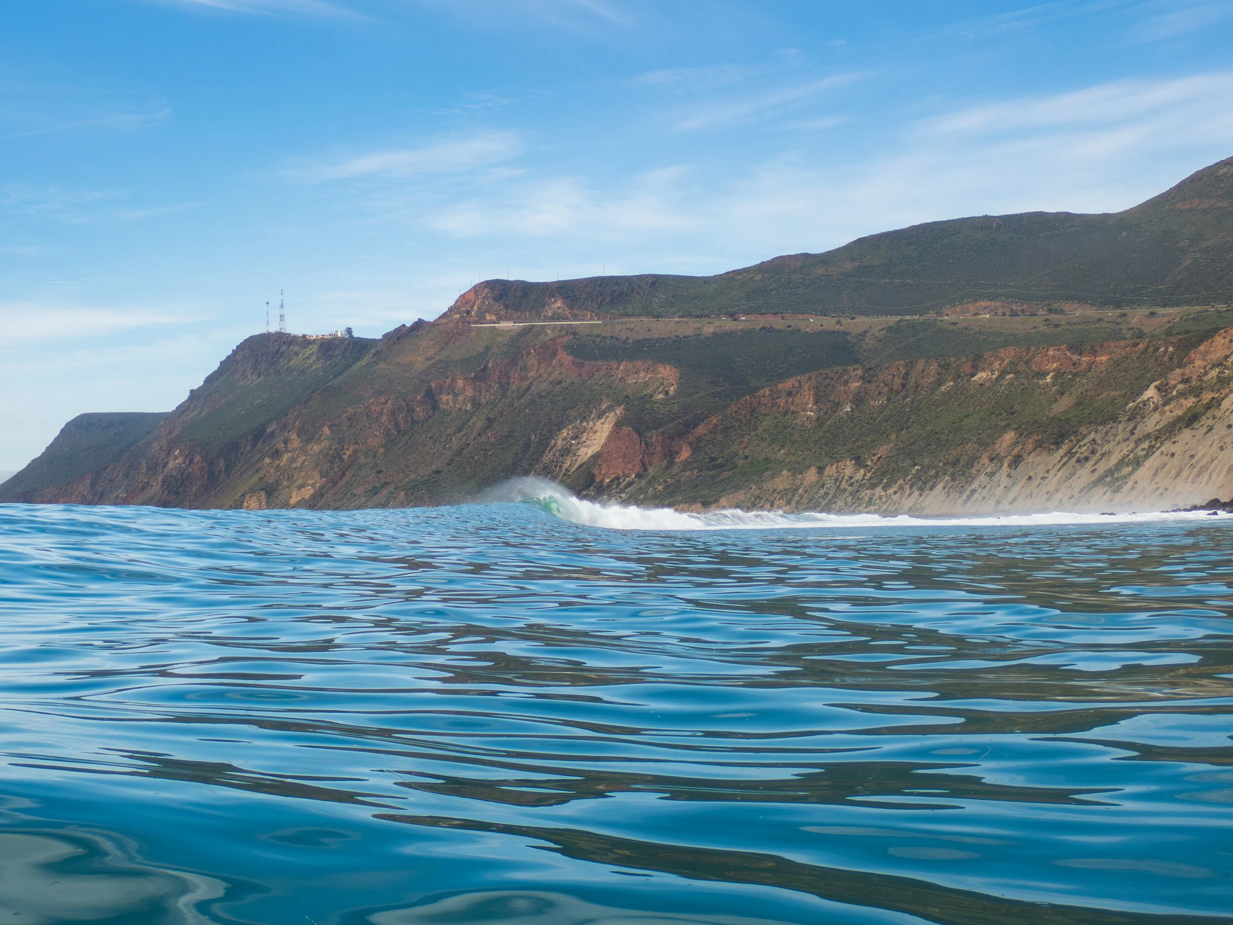Ocean water with hills and mountains in the background under a partly cloudy sky.