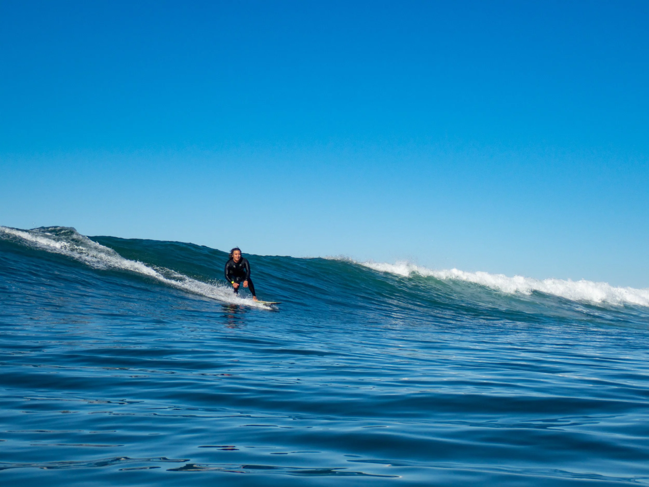 A person surfing on a wave in the ocean with a clear blue sky in the background.