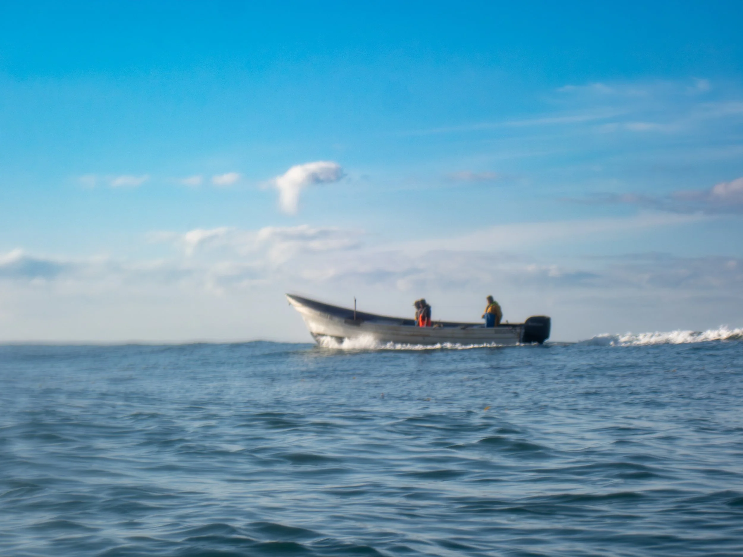 A boat with two people on the open water under a partly cloudy sky.