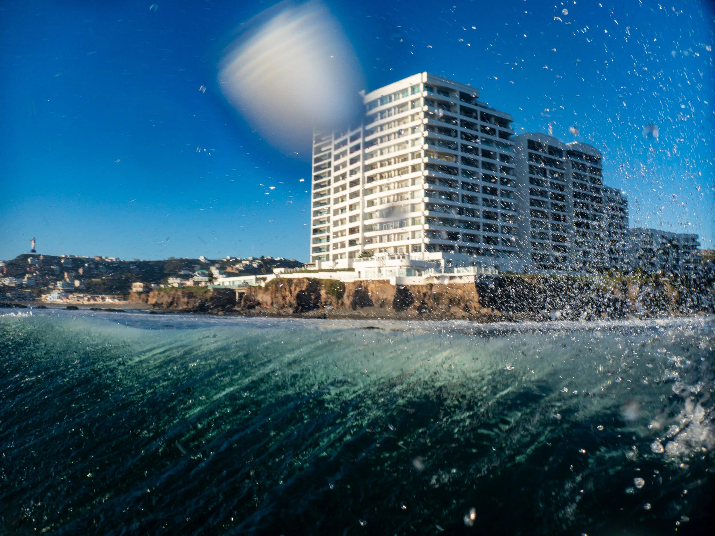 View of a high-rise building near the ocean with a water splash in the foreground and a clear blue sky