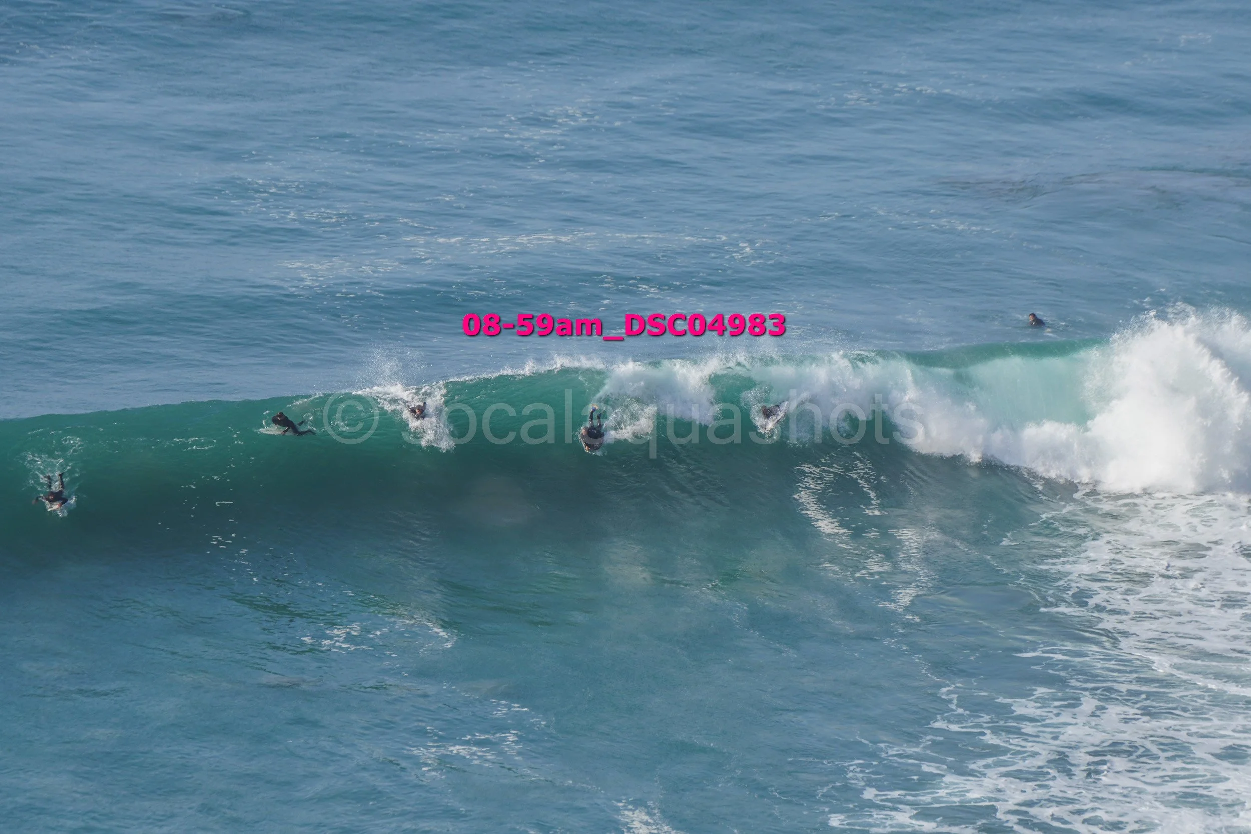 Several surfers in wetsuits riding and swimming in ocean waves with blue water and white foam.
