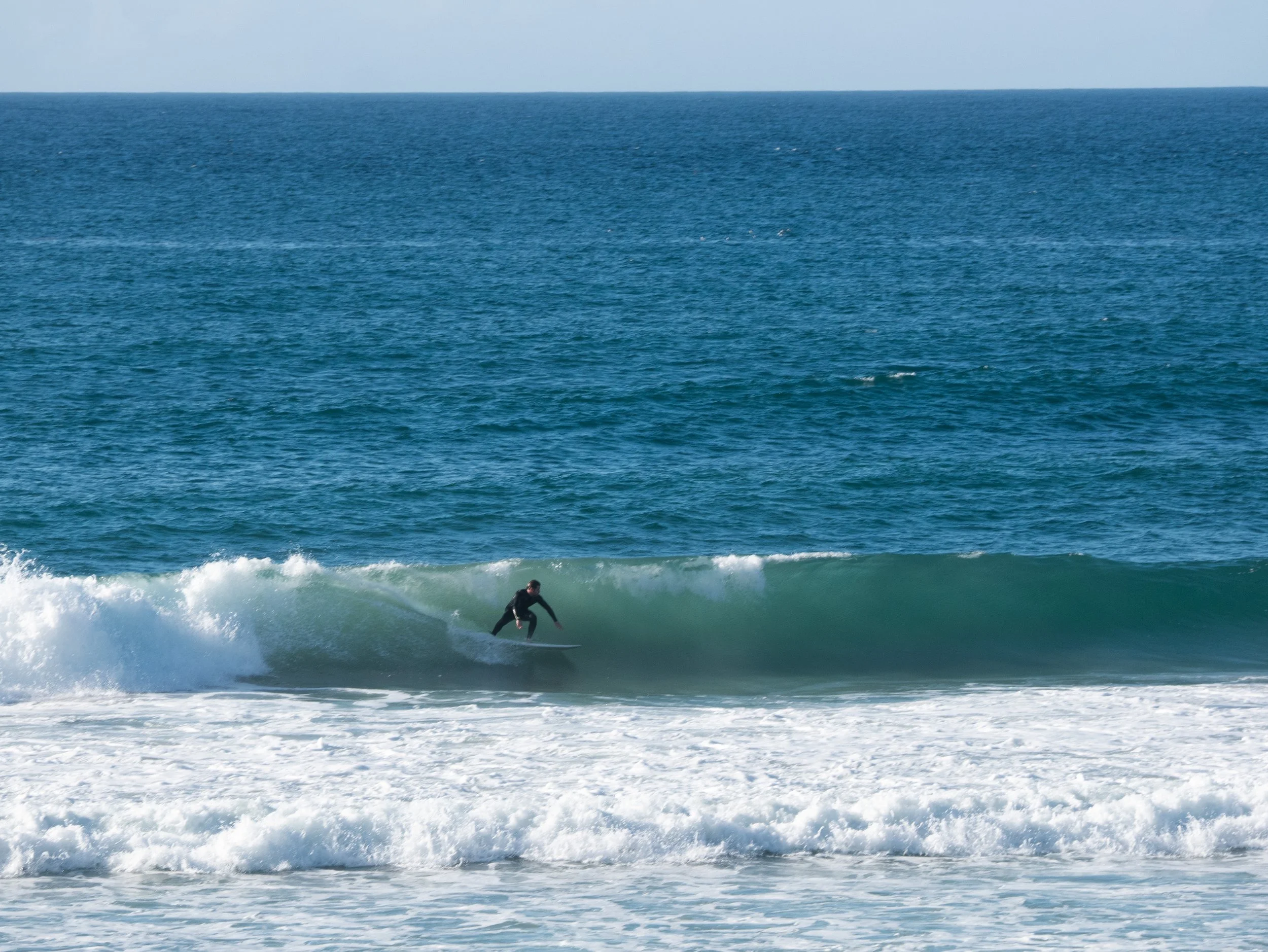 A person surfing on a wave in the ocean with blue water and clear sky.