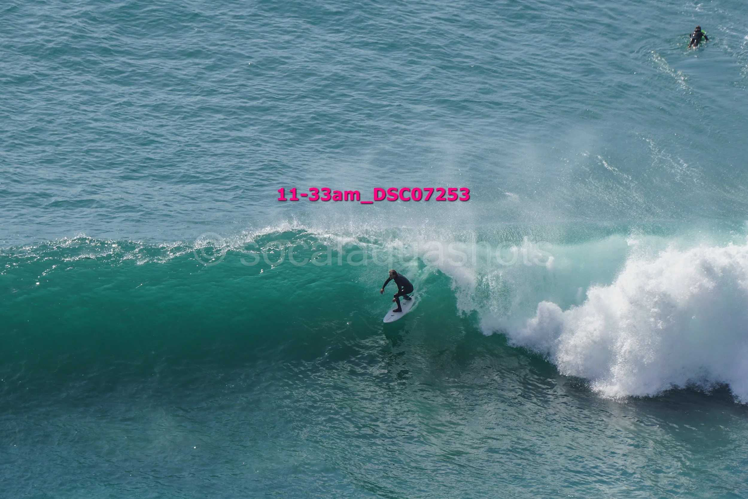 A person surfing on a wave in the ocean during daytime, with another person in the water nearby.