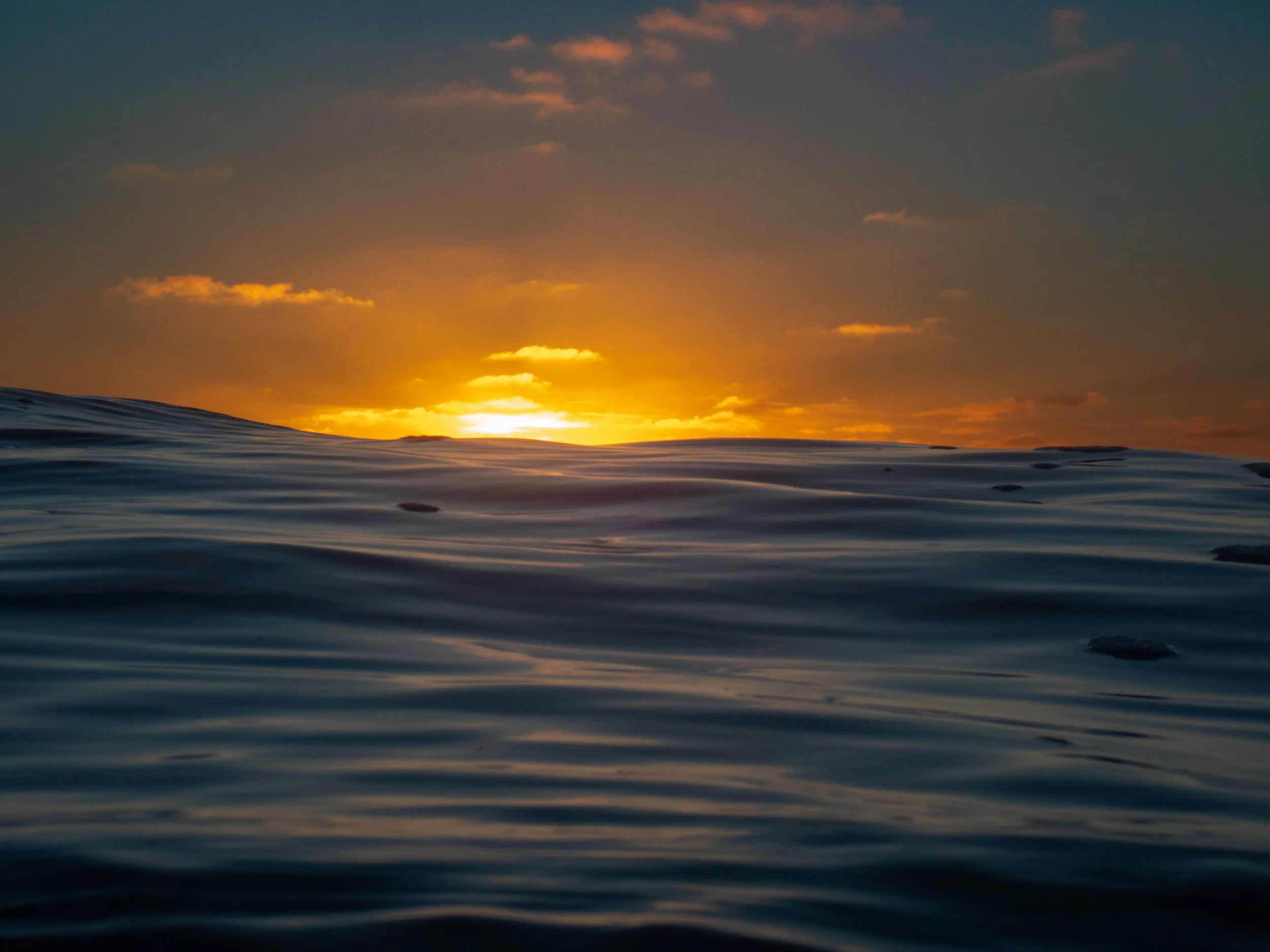 Sunset over the ocean with calm water and a few clouds in the sky.
