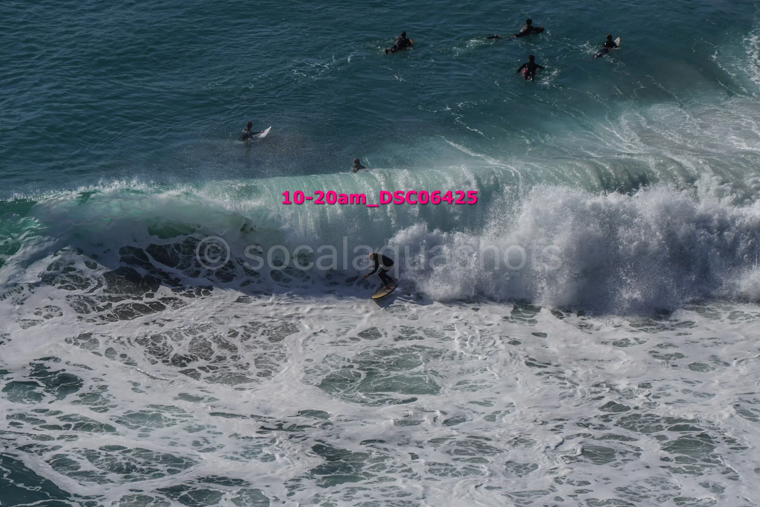 Surfer riding a wave with multiple surfers in the water in the background.