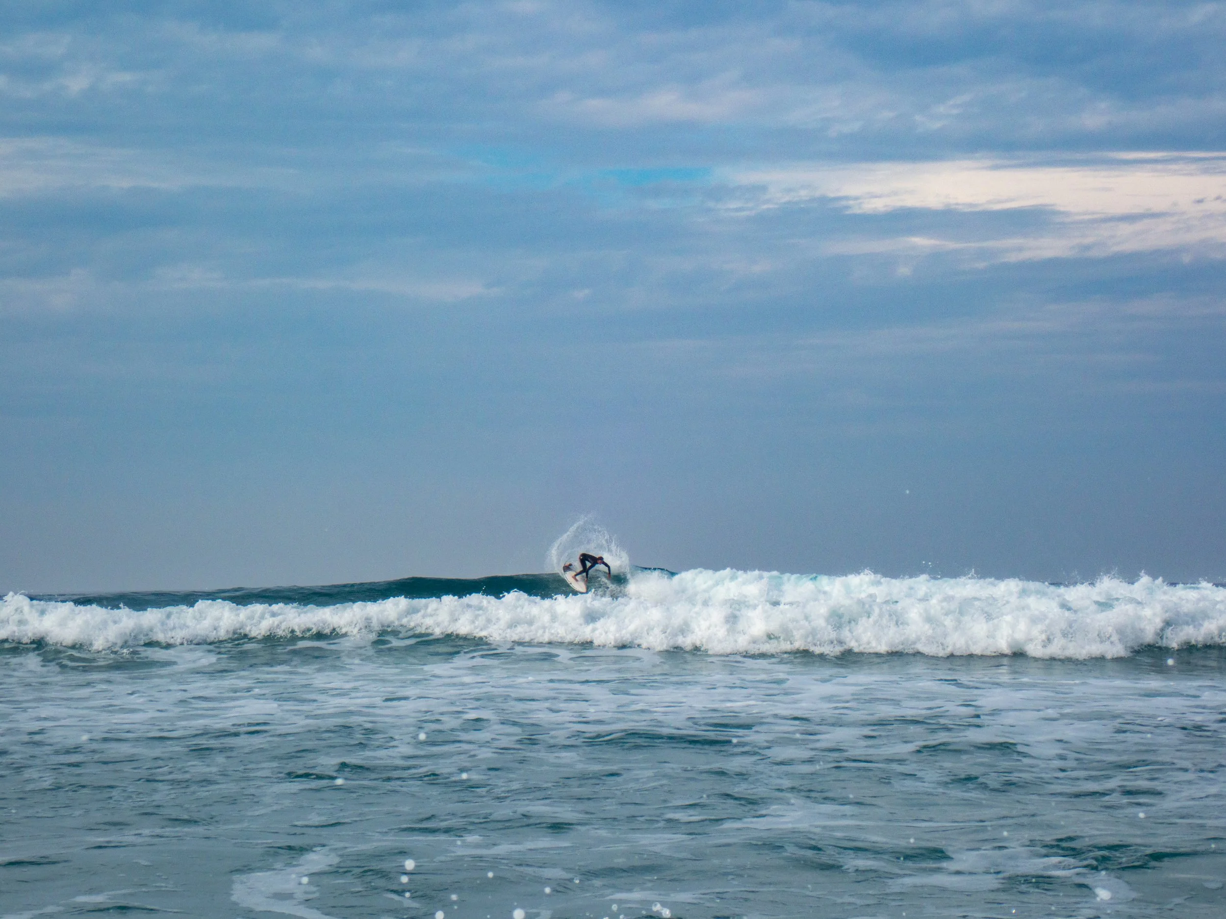 A surfer riding a wave in the ocean under a partly cloudy sky.