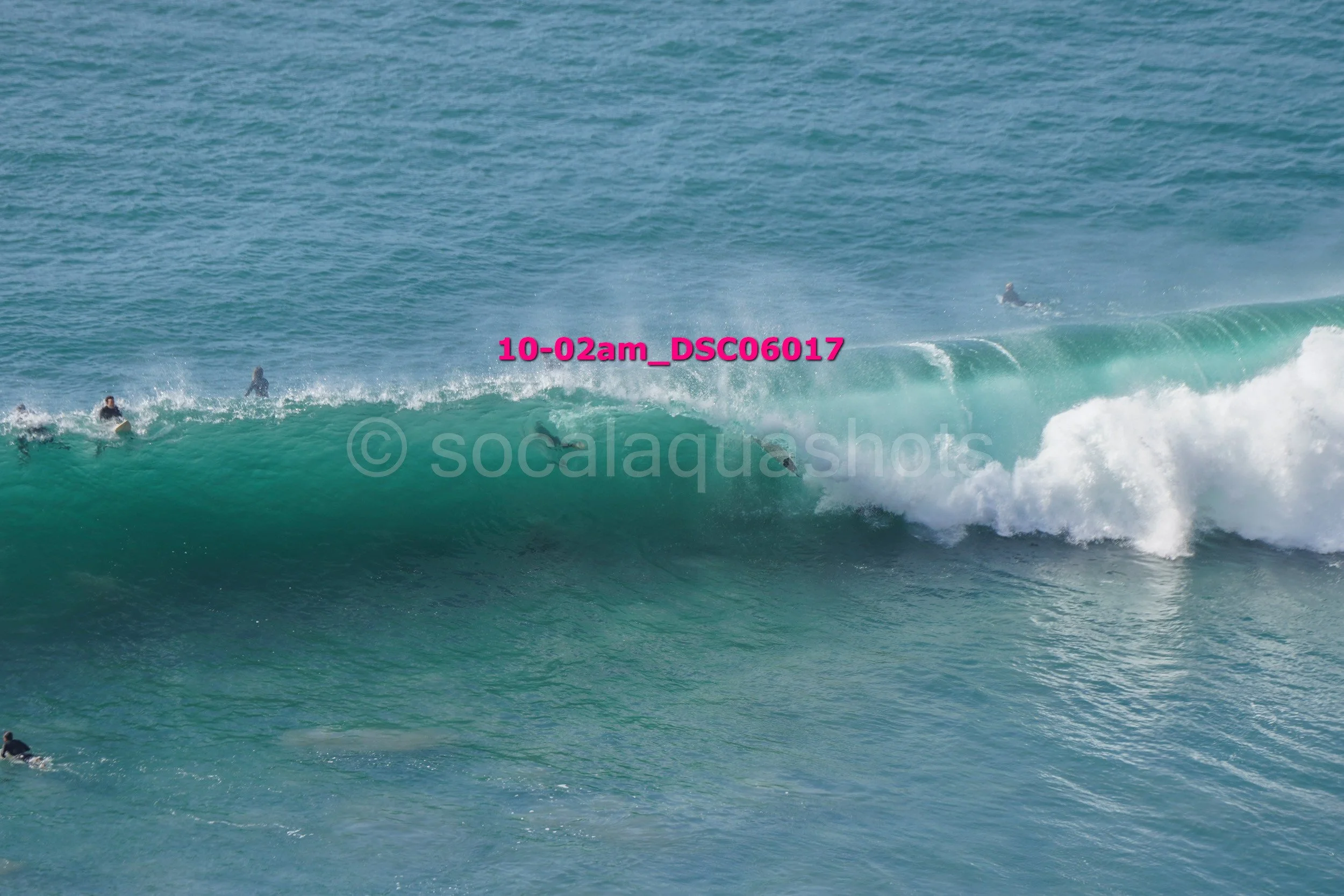 Surfers riding a large ocean wave with some surfers in the background and in the water.
