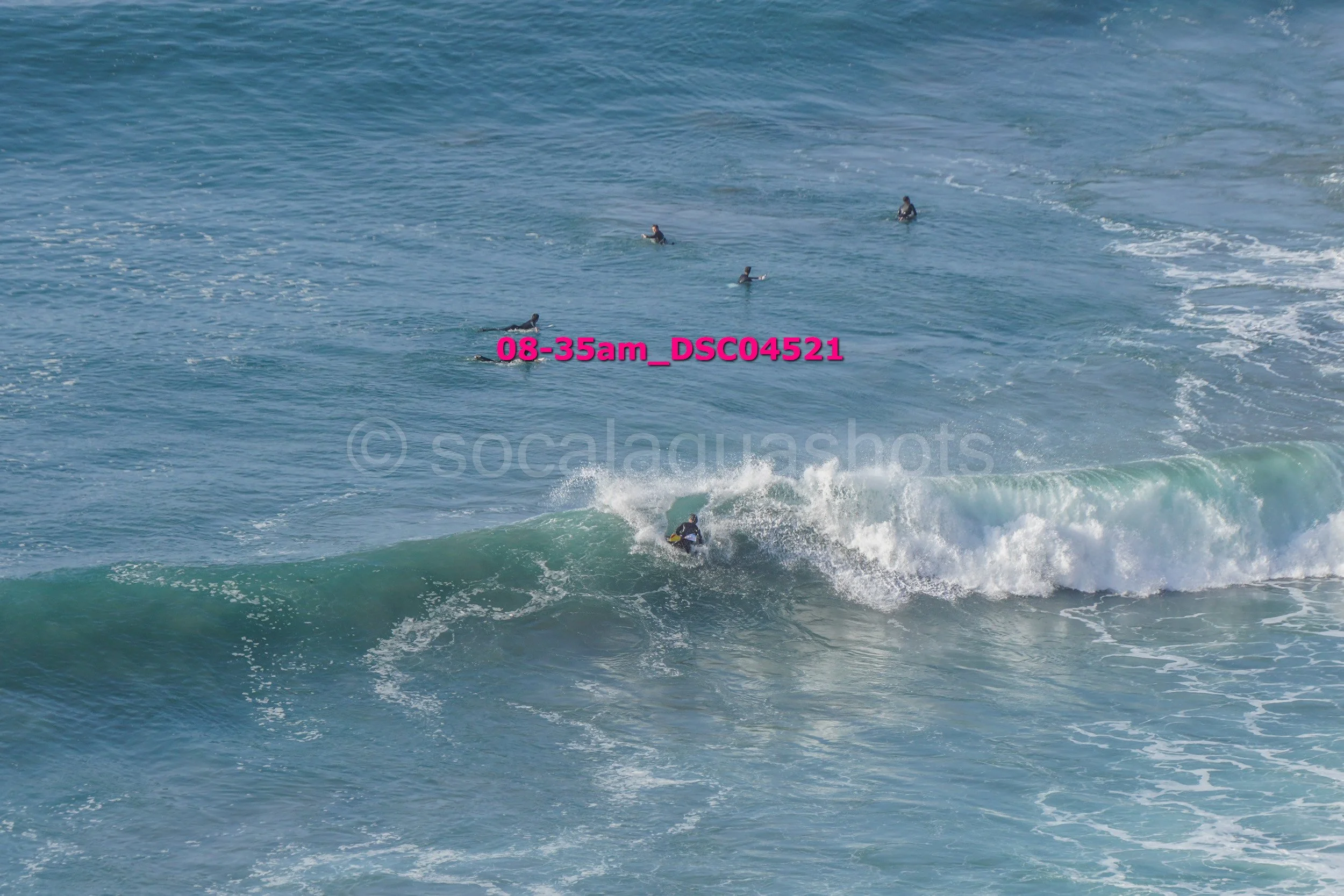 Surfer riding a wave in the ocean with several people in the water in the background.