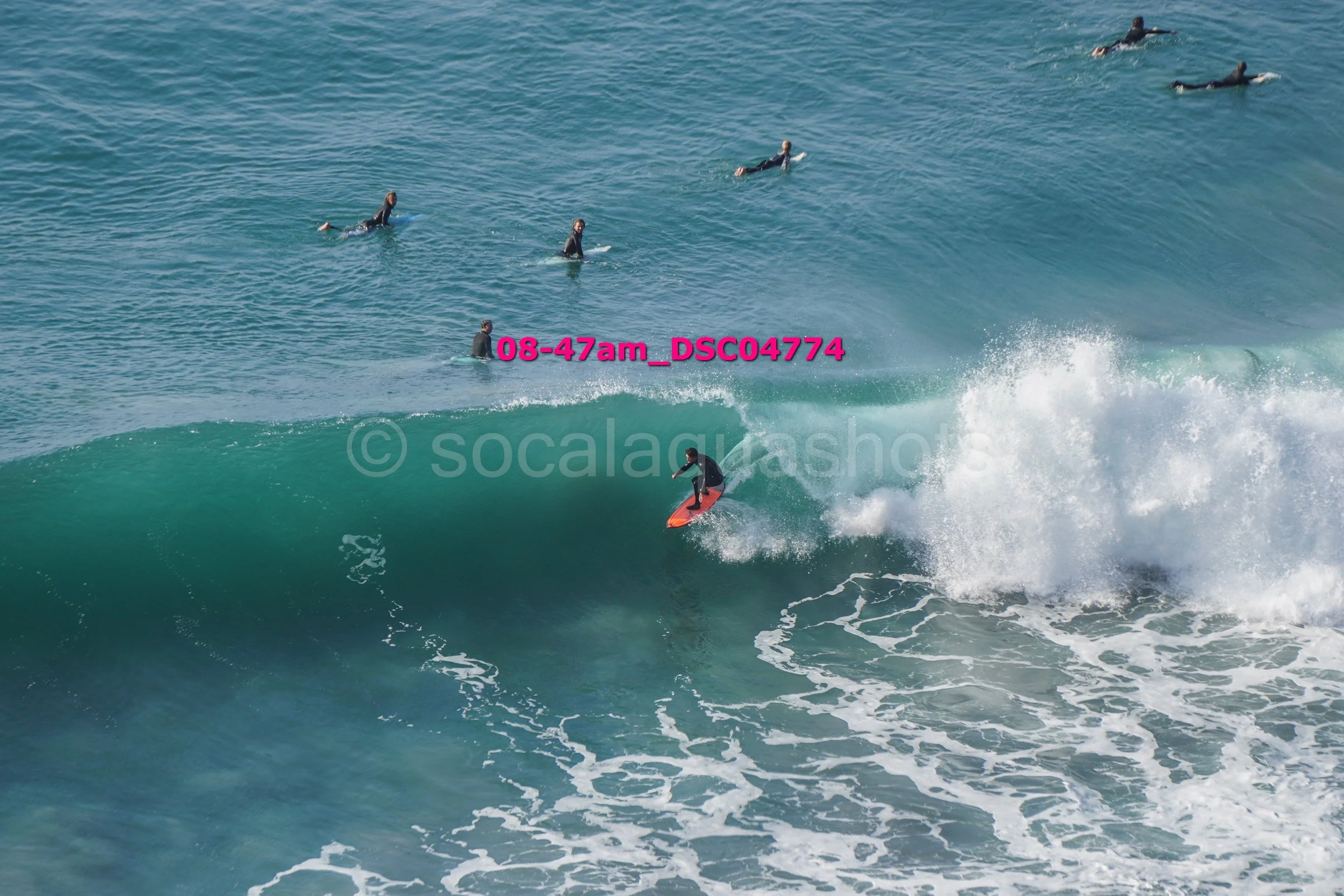 Surfer riding a wave with several people swimming in the ocean in the background.