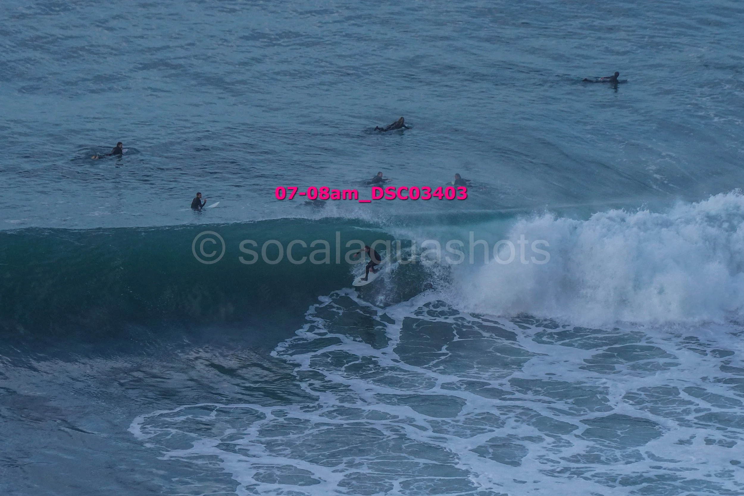 Surfer riding a wave with several people on surfboards in the water in the background.