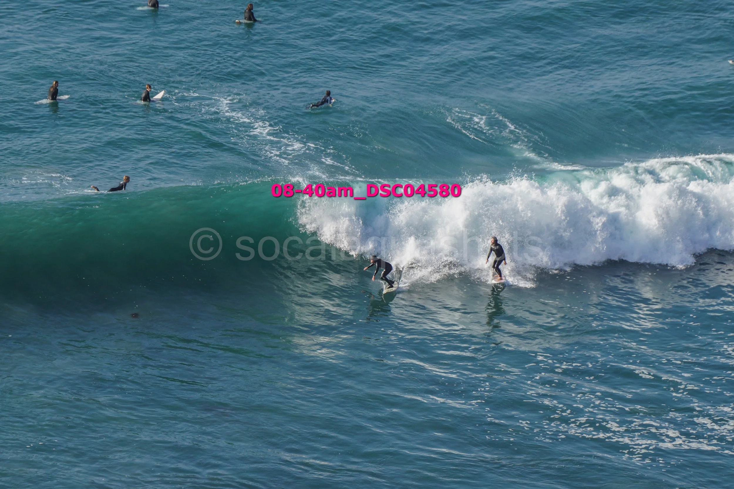 Multiple surfers surfing on waves in the ocean, with some standing and others riding the waves.