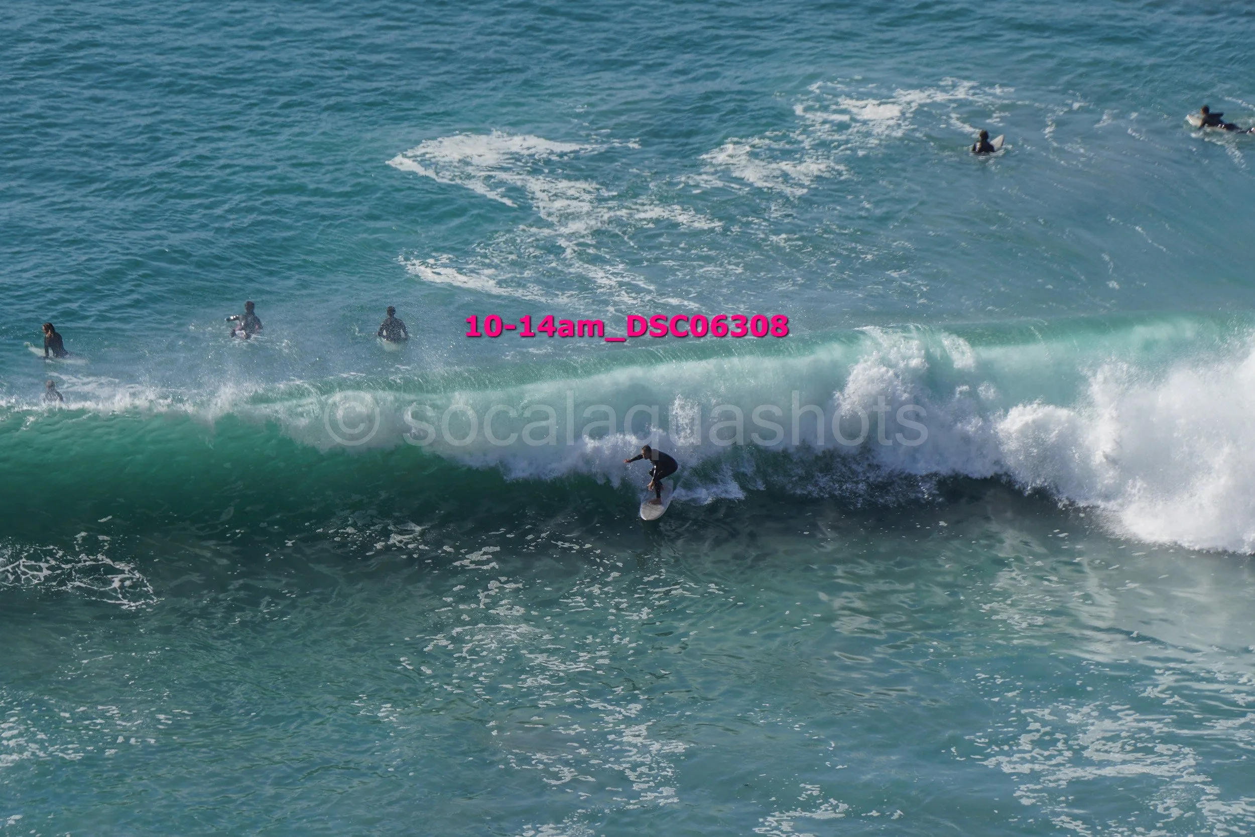 A person surfing on a wave in the ocean with multiple people swimming nearby.