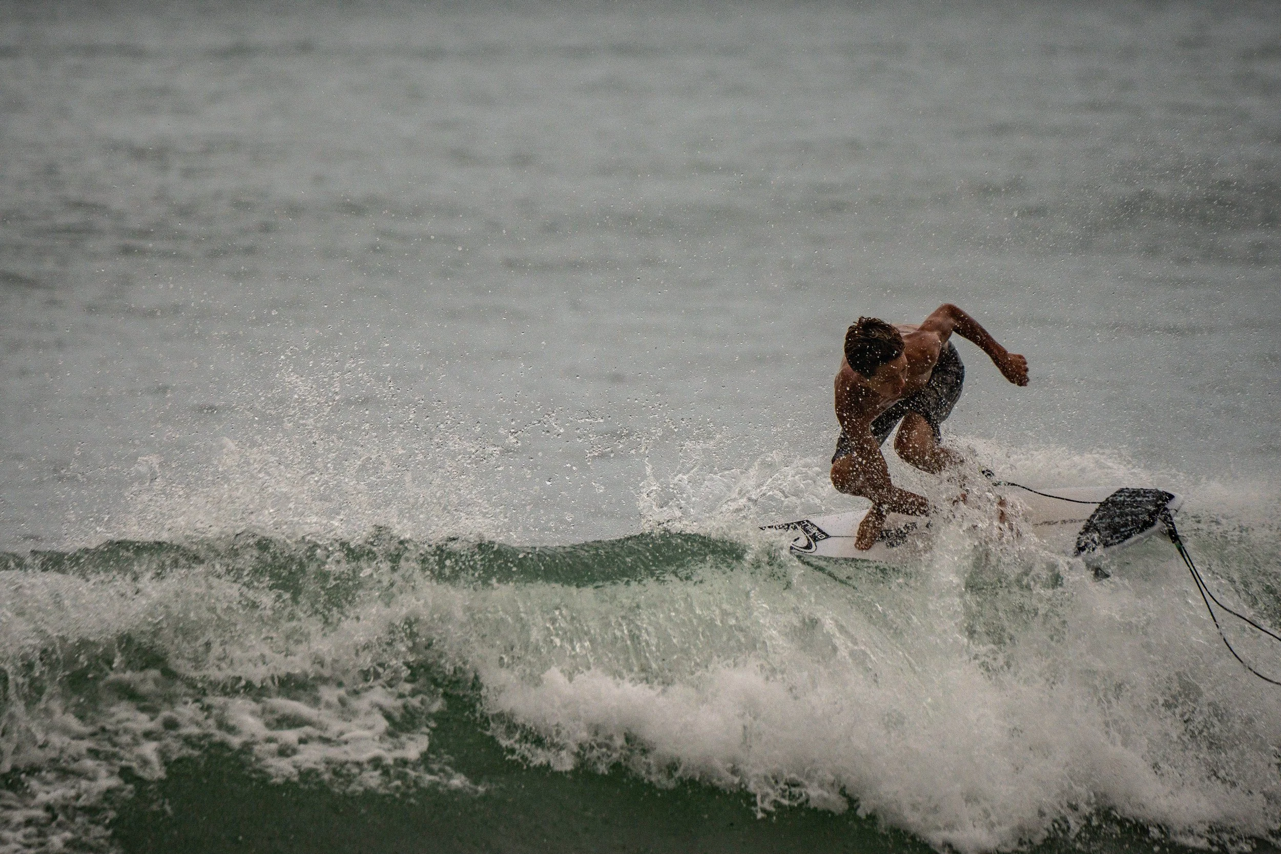 A person wearing black swim shorts is riding a wakeboard on a wave at the beach.