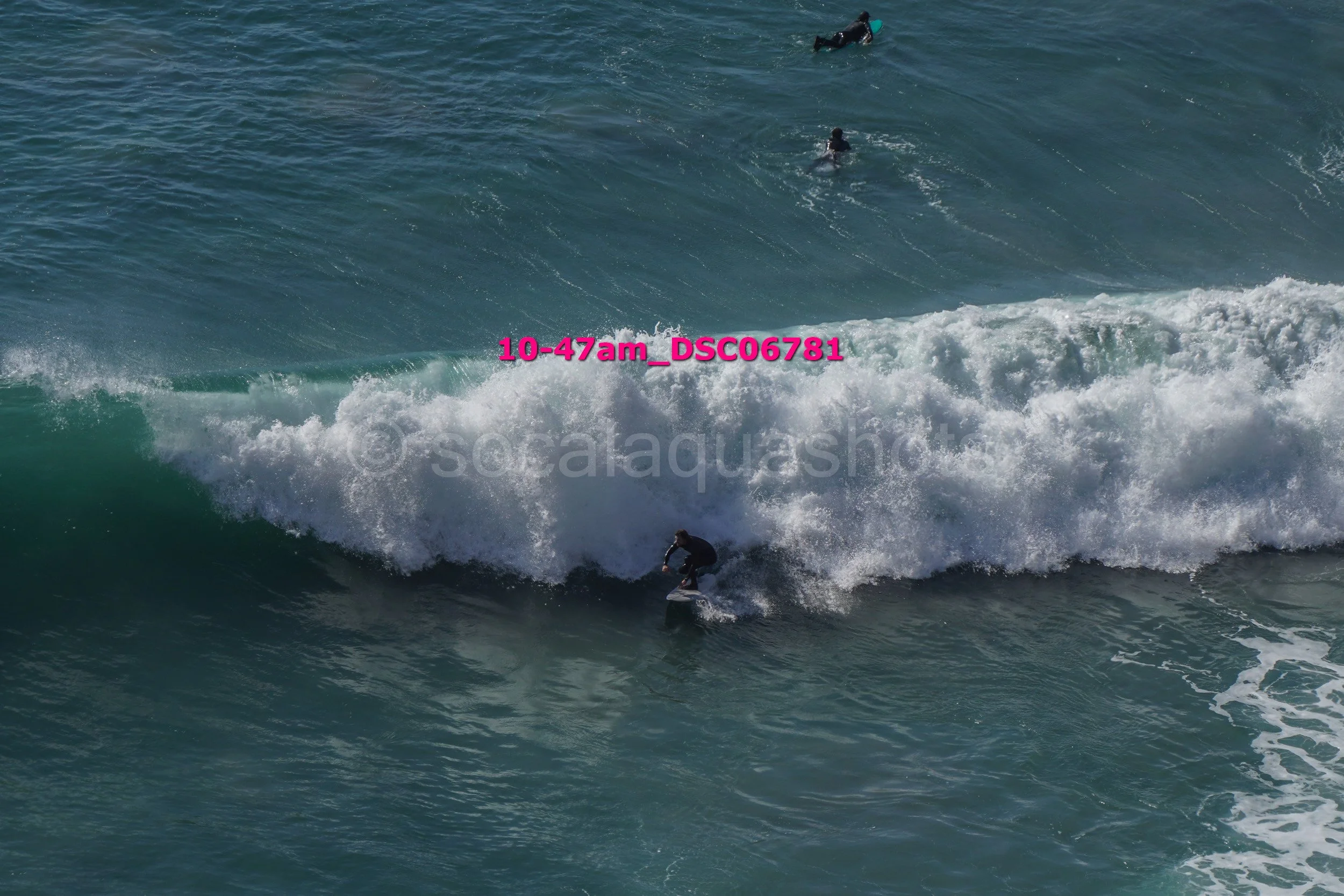 Surfer riding a wave with two people swimming in the background in the ocean.