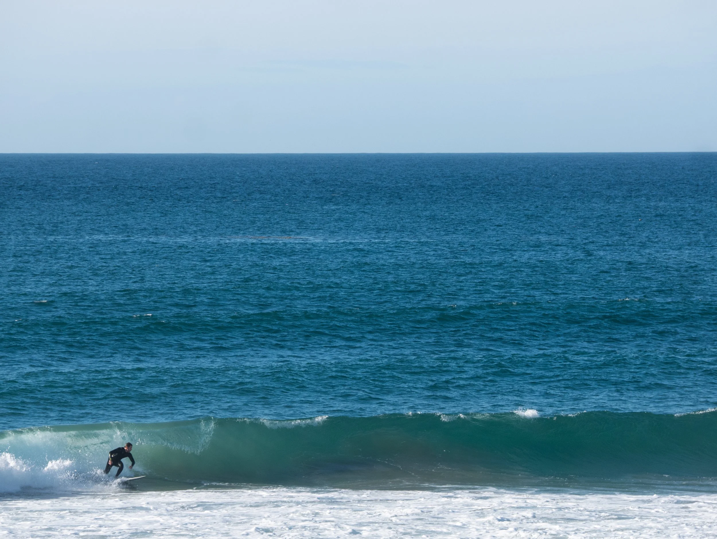 A person surfing on a wave in the ocean with a clear blue sky above.